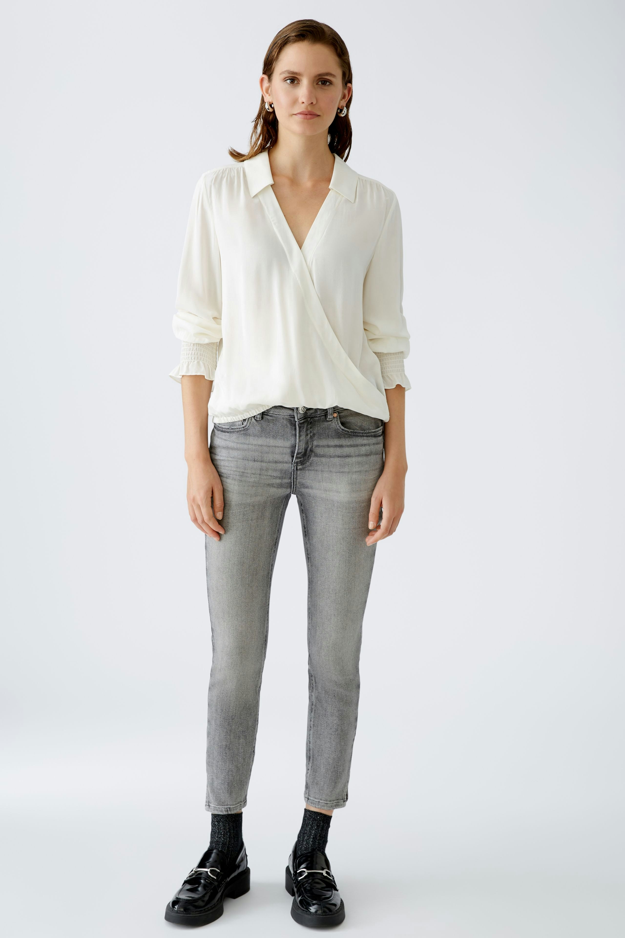 Elegant women's blouse: A woman in a white wrap blouse paired with gray jeans, exuding effortless style.