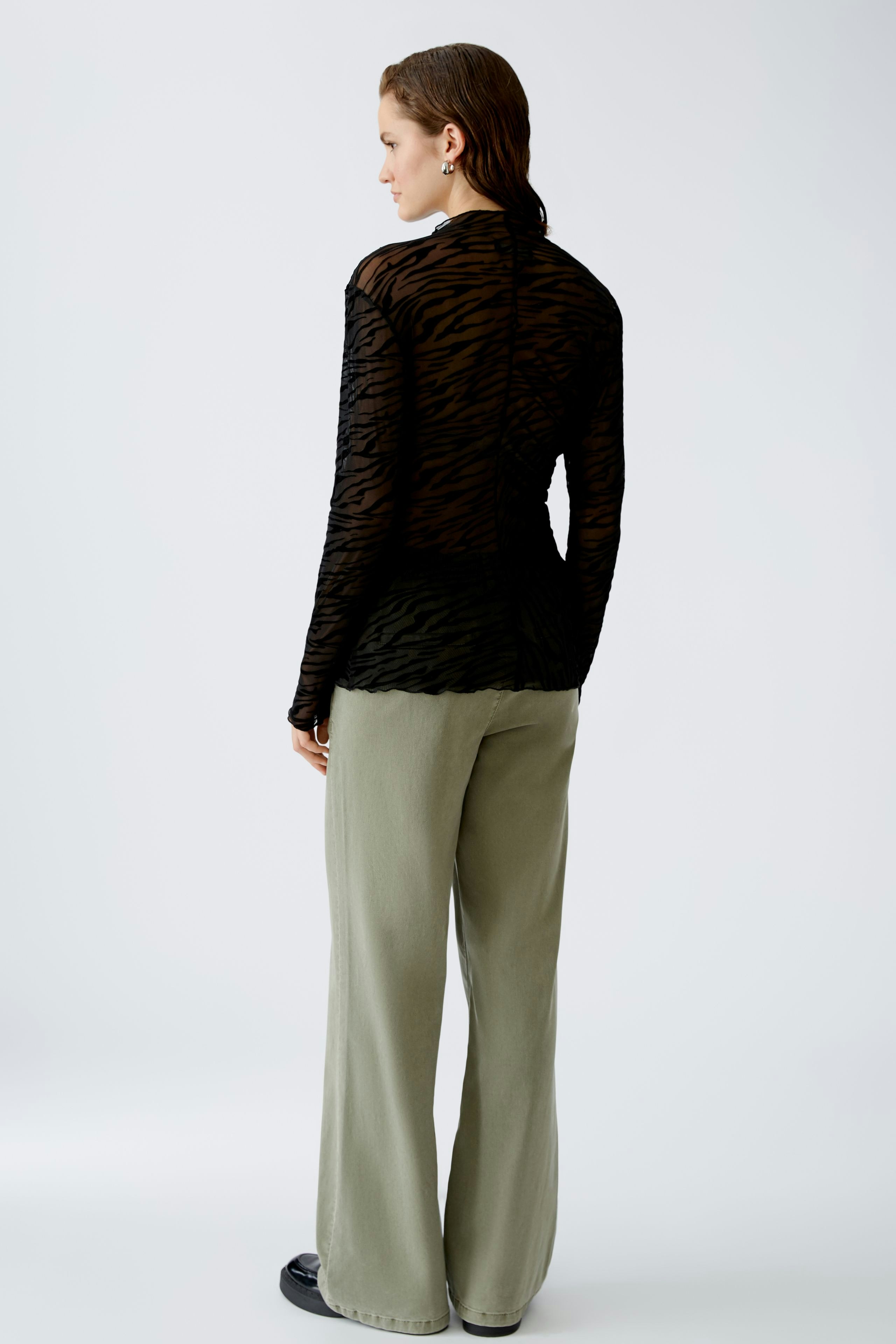 Stylish long-sleeve shirt: Woman in a black sheer top with a subtle animal print, paired with relaxed trousers.