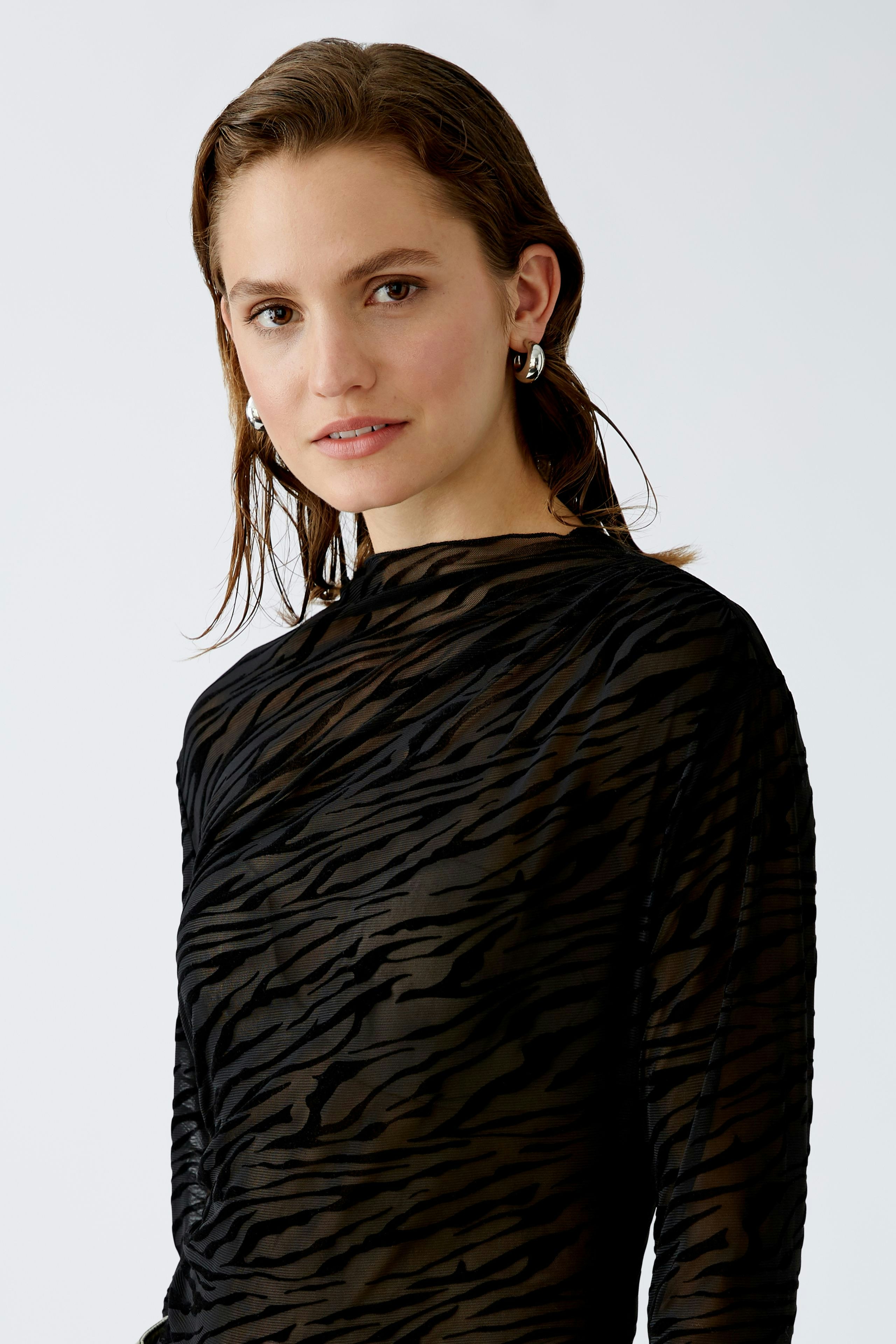 Elegant long-sleeve shirt: A woman in a black, sheer shirt with a subtle tiger print.