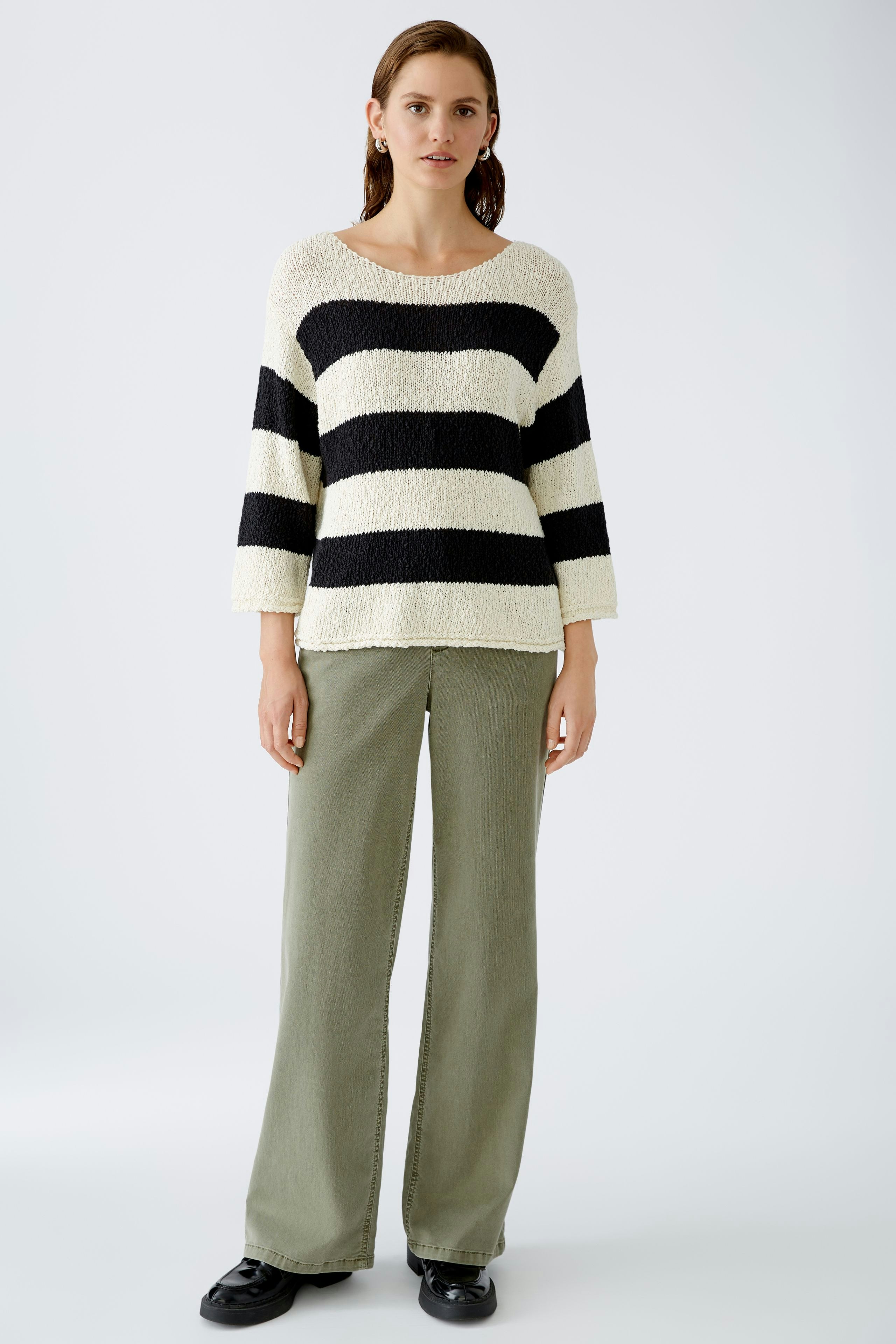 Stylish women's pullover: A woman in a striped pullover with black and cream colors, paired with relaxed pants.