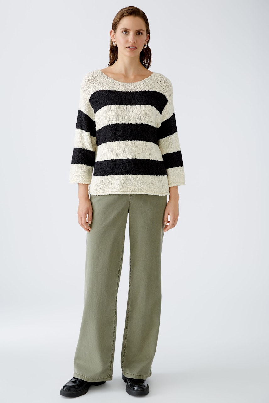 Stylish women's pullover: A woman in a striped pullover with black and cream colors, paired with relaxed pants.