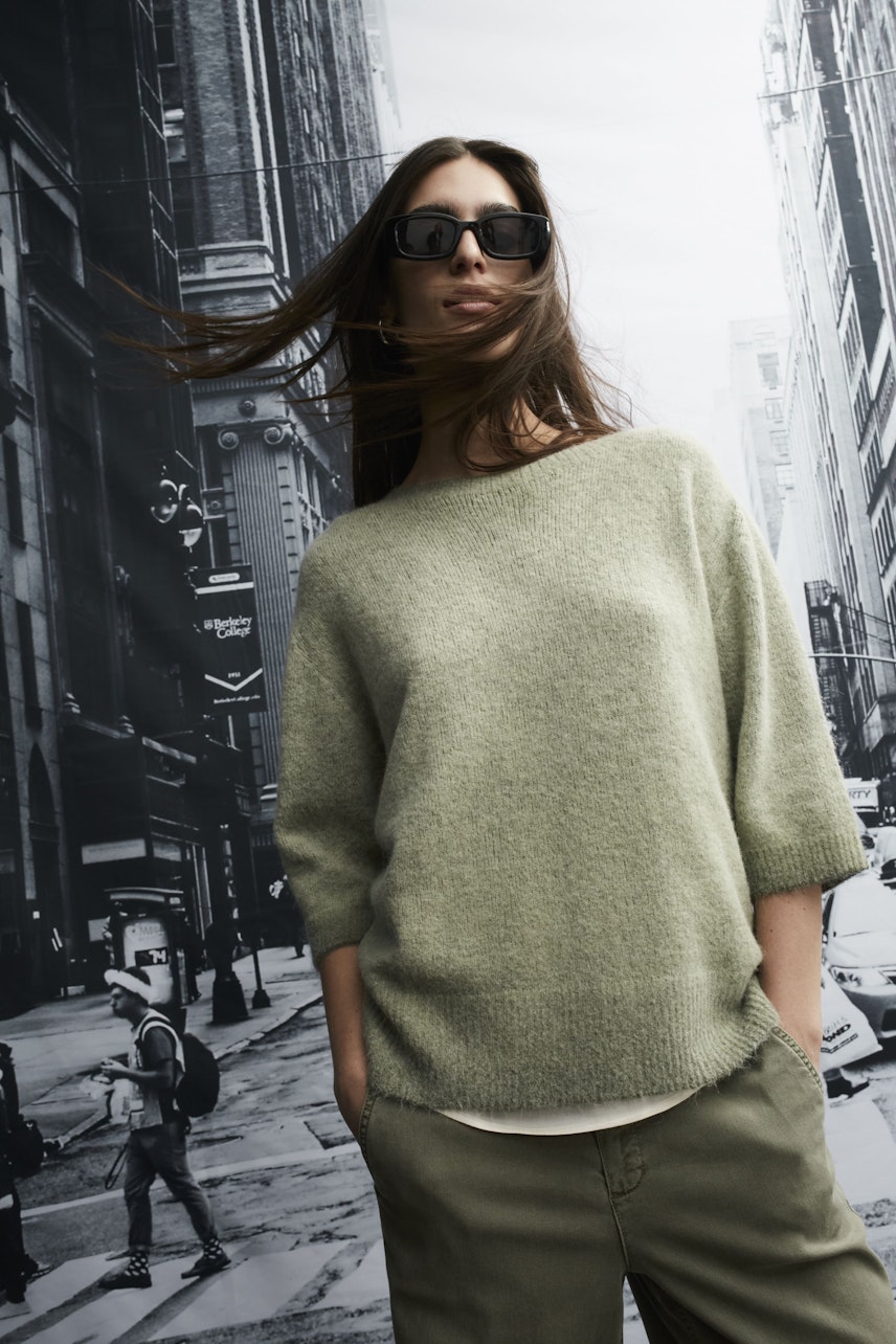 Modern women's pullover: A woman in a light green pullover with a relaxed fit poses confidently.