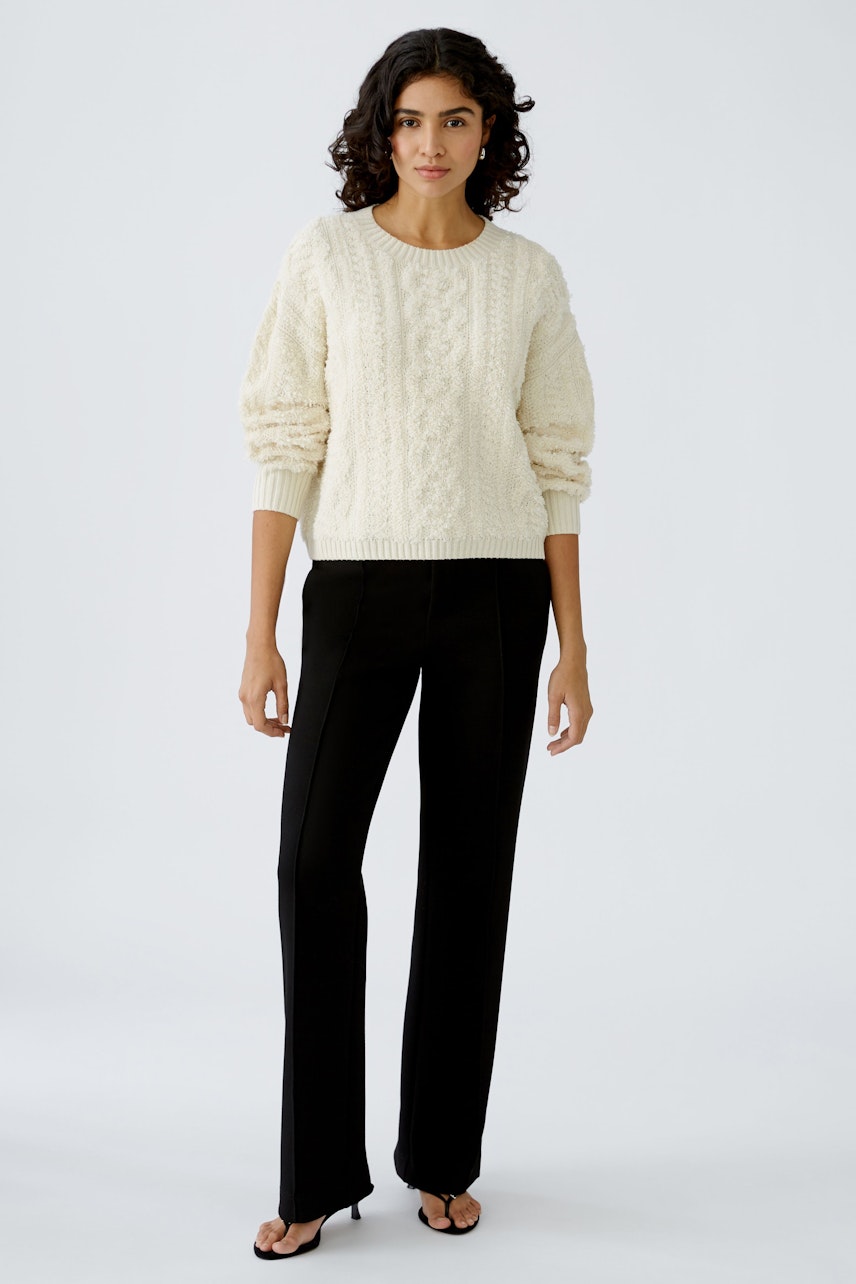 Stylish women's pullover: A woman in a cream cable-knit pullover paired with sleek black trousers.