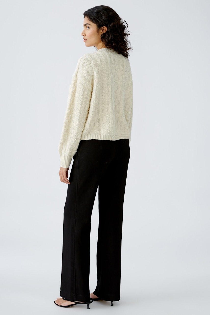 Stylish women's pullover: A woman in a cozy cream pullover with textured knit, paired with black pants.