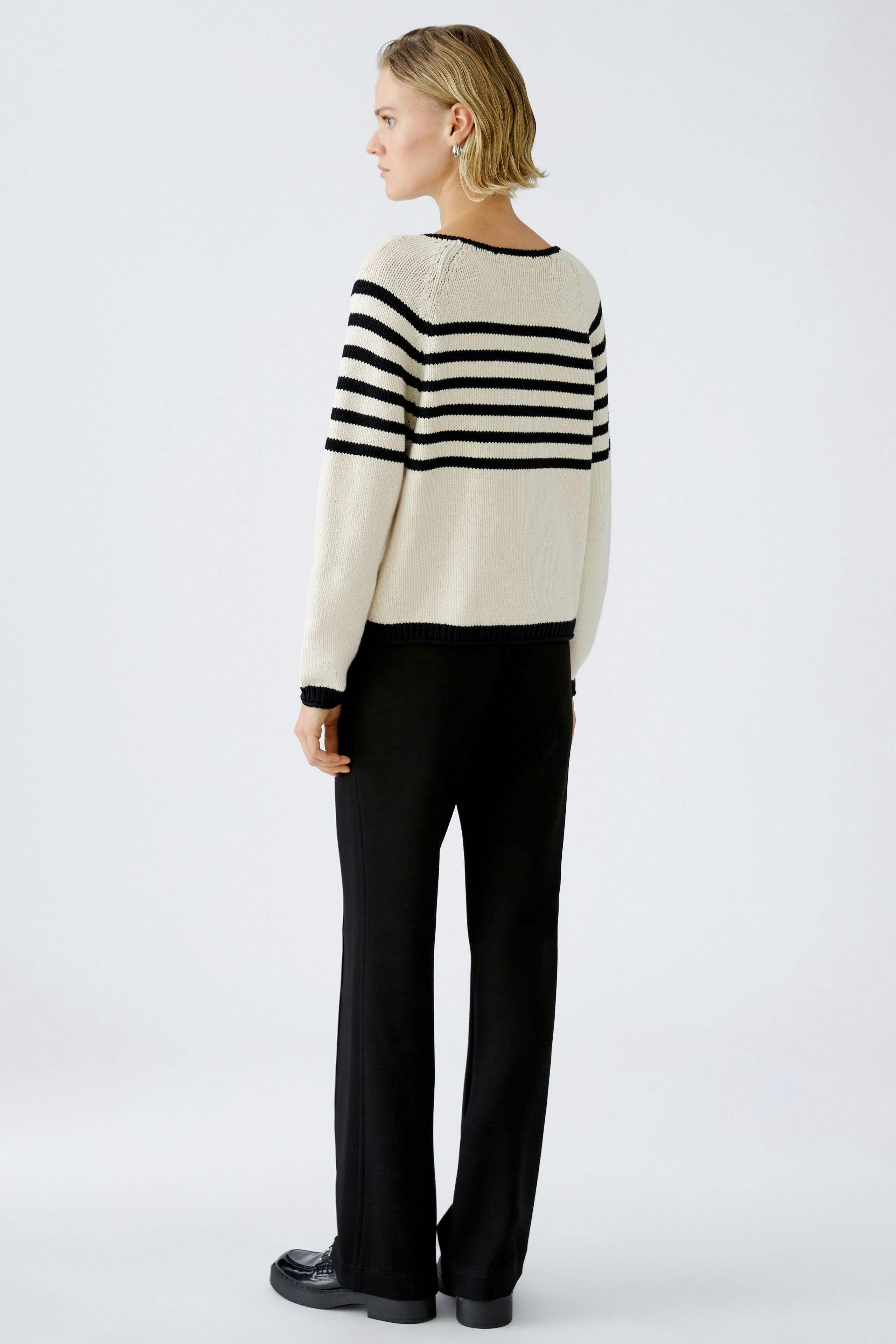 Damen-Pullover: Frau trägt einen beigen Pullover mit schwarzen Streifen und lässigen Hosen.