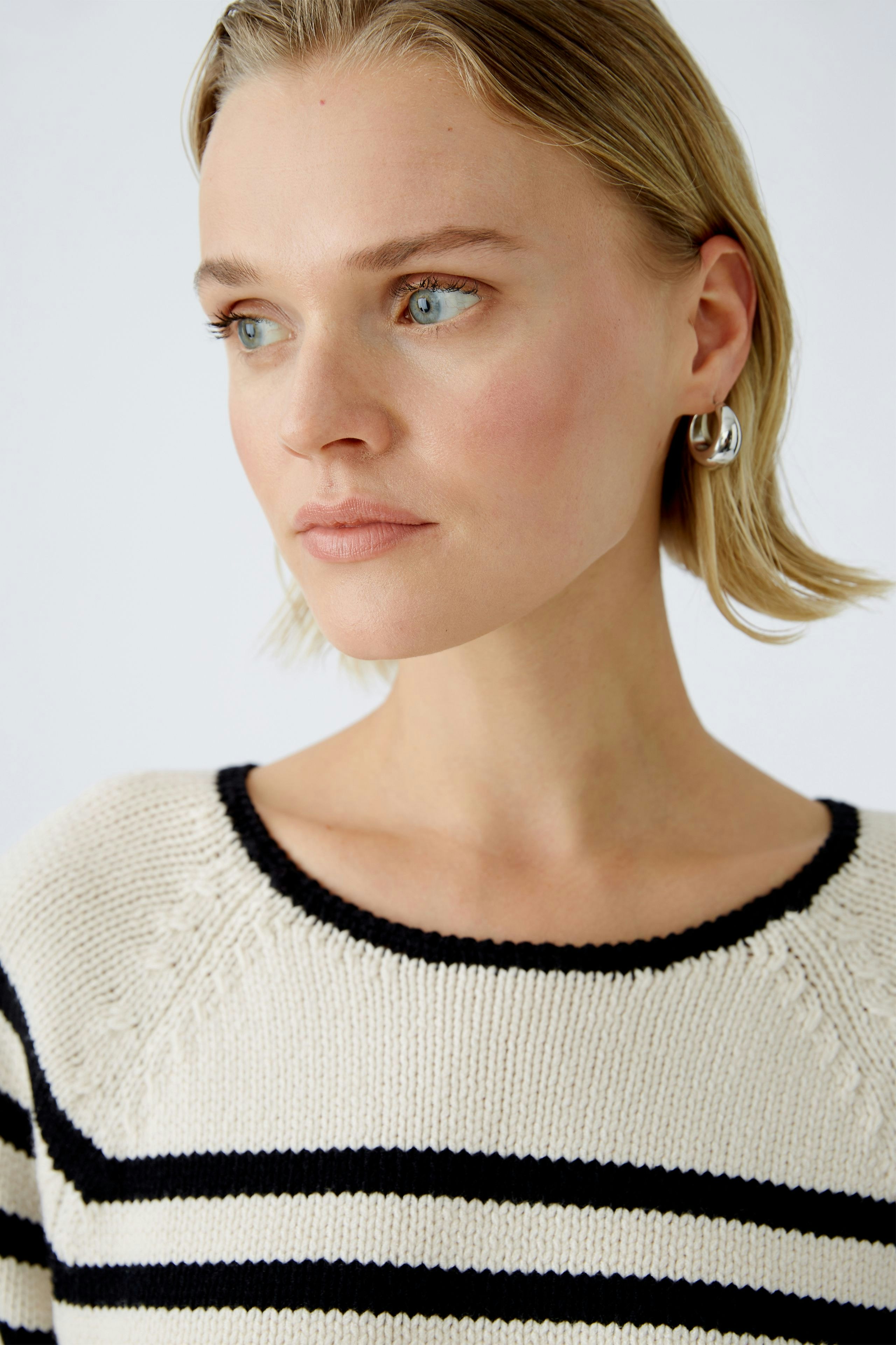 Damen-Pullover: Frau mit gestreiftem Pullover in Creme und Schwarz, lässig und modern.