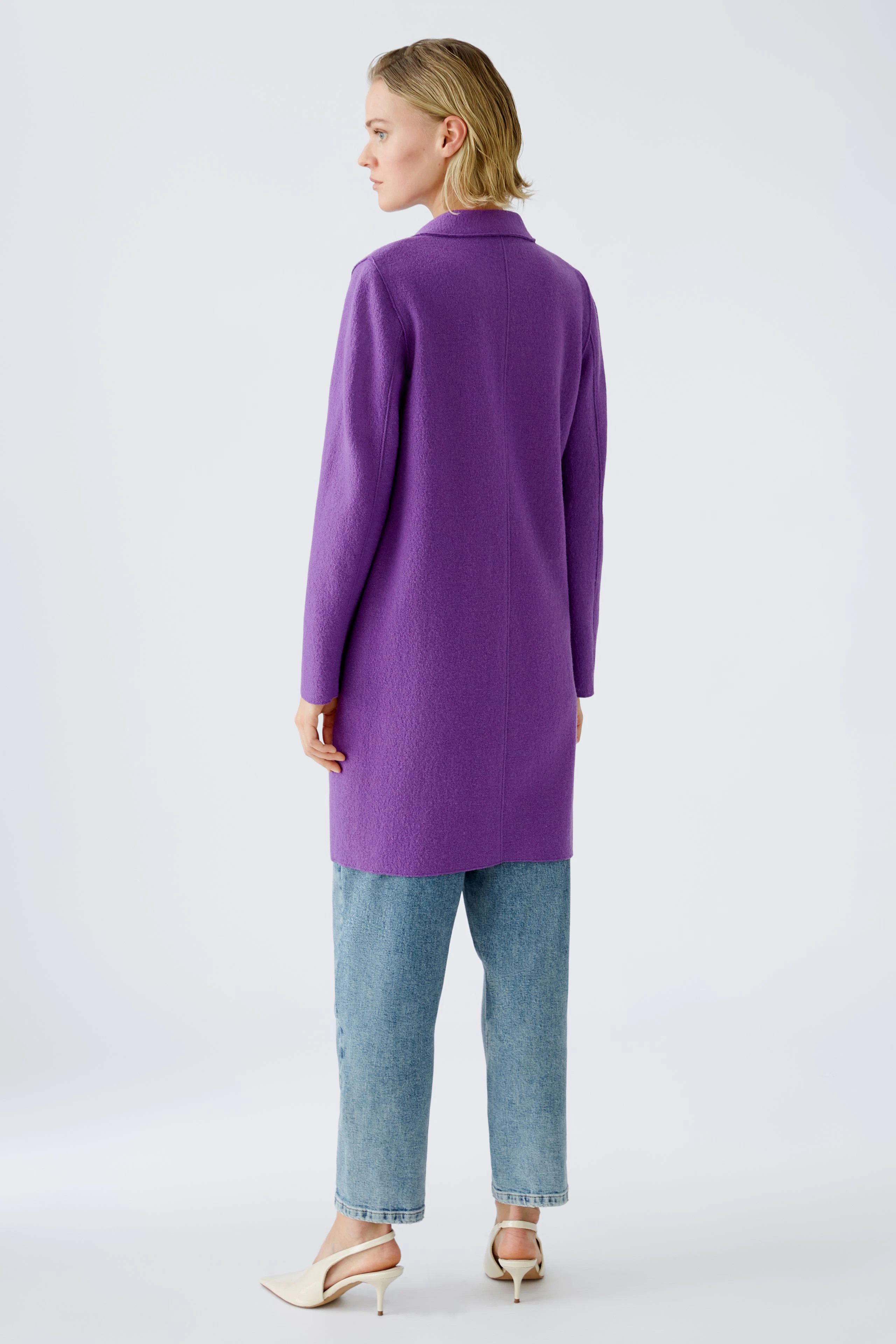 Eleganter Wollmantel: Frau in lila Wollmantel mit lässigen Jeans und eleganten Schuhen von hinten.
