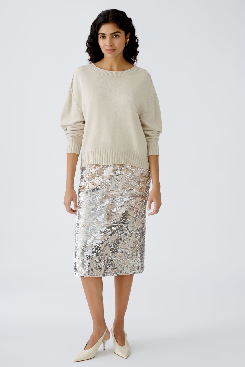 Modern women's pullover: A woman in a cream pullover paired with a shimmering silver skirt.