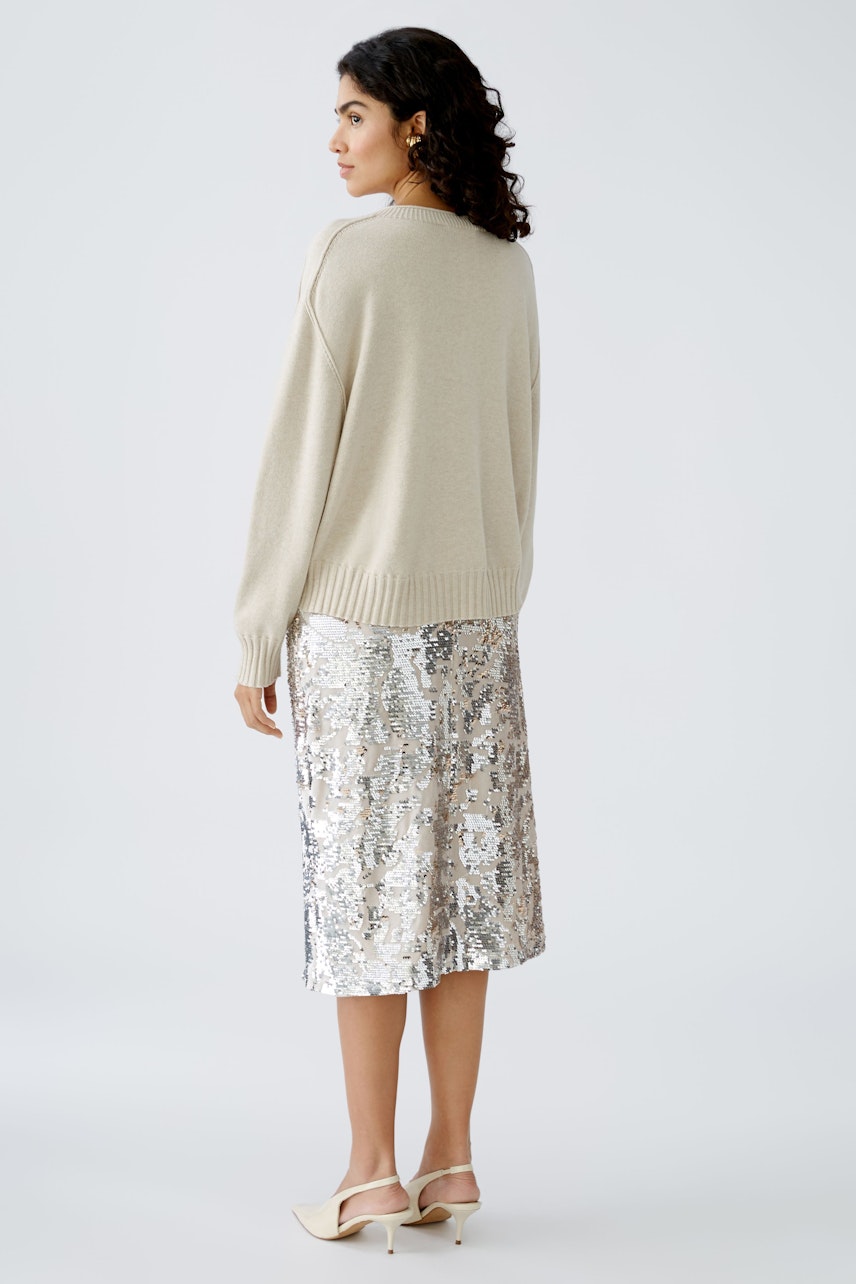 Elegant women's pullover in soft beige, paired with a shimmering silver skirt, showcasing a stylish look.