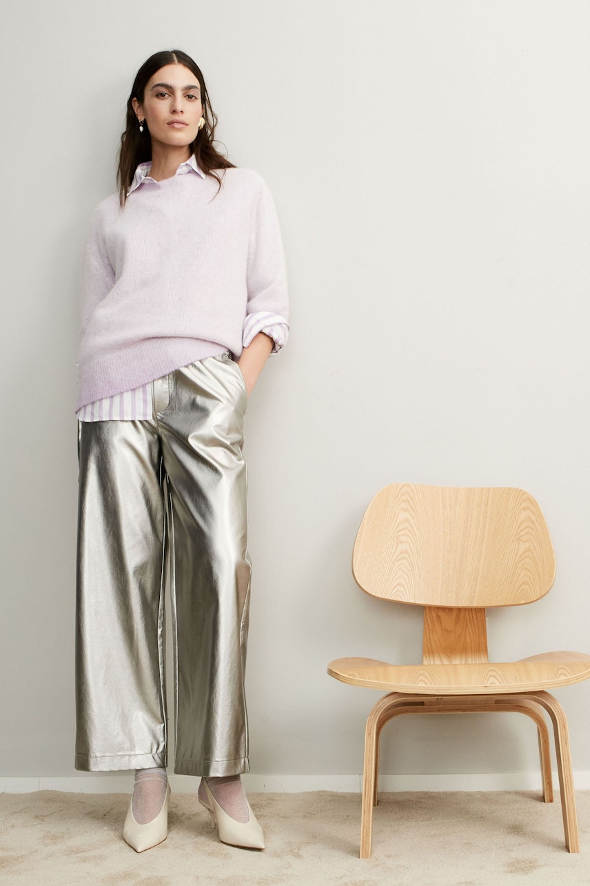 Modern women's pullover: A woman in a light purple pullover paired with shiny silver pants.