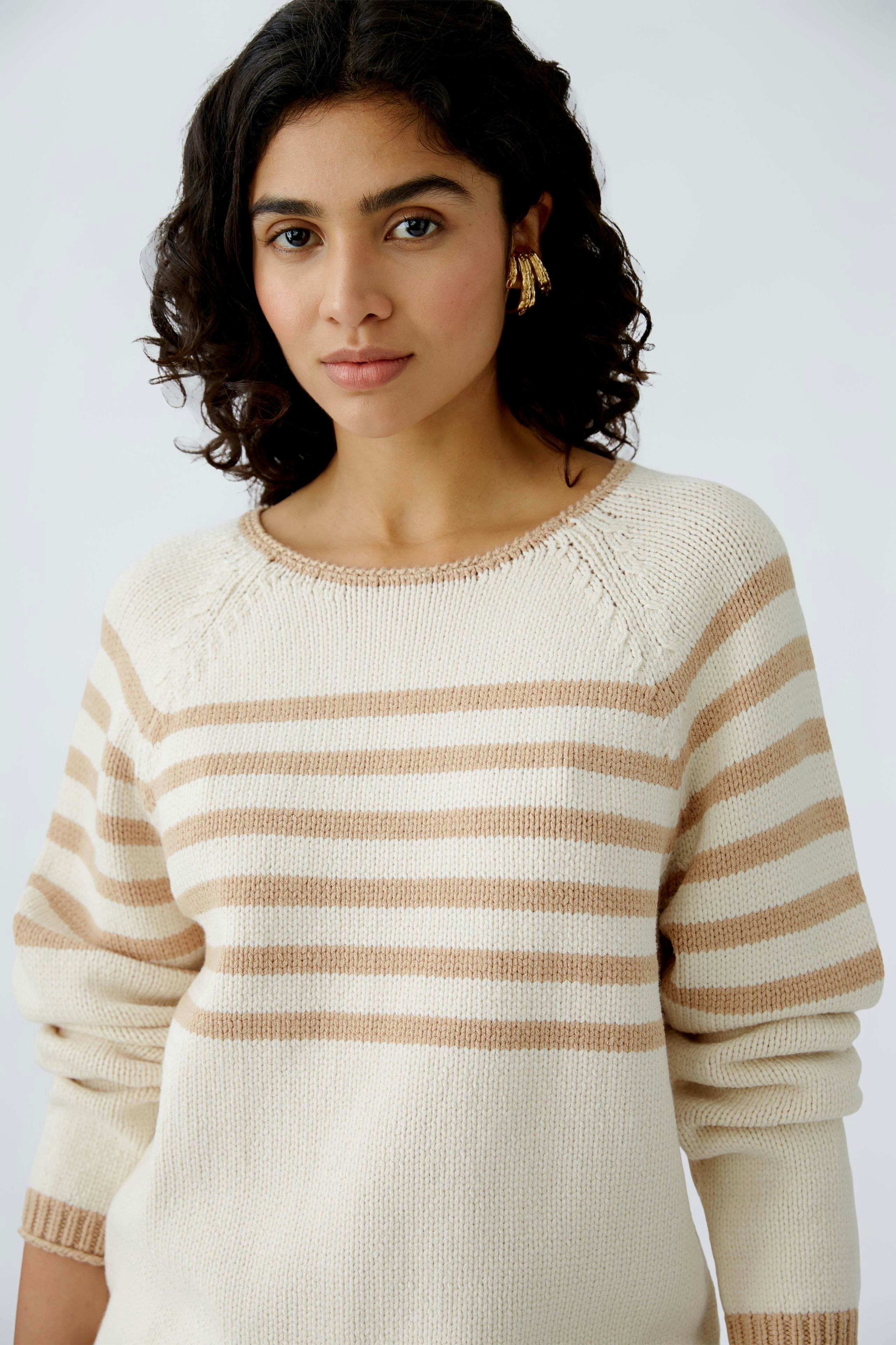Damen-Pullover: Frau in cremefarbenem Pullover mit beigen Streifen, lässig und modern.