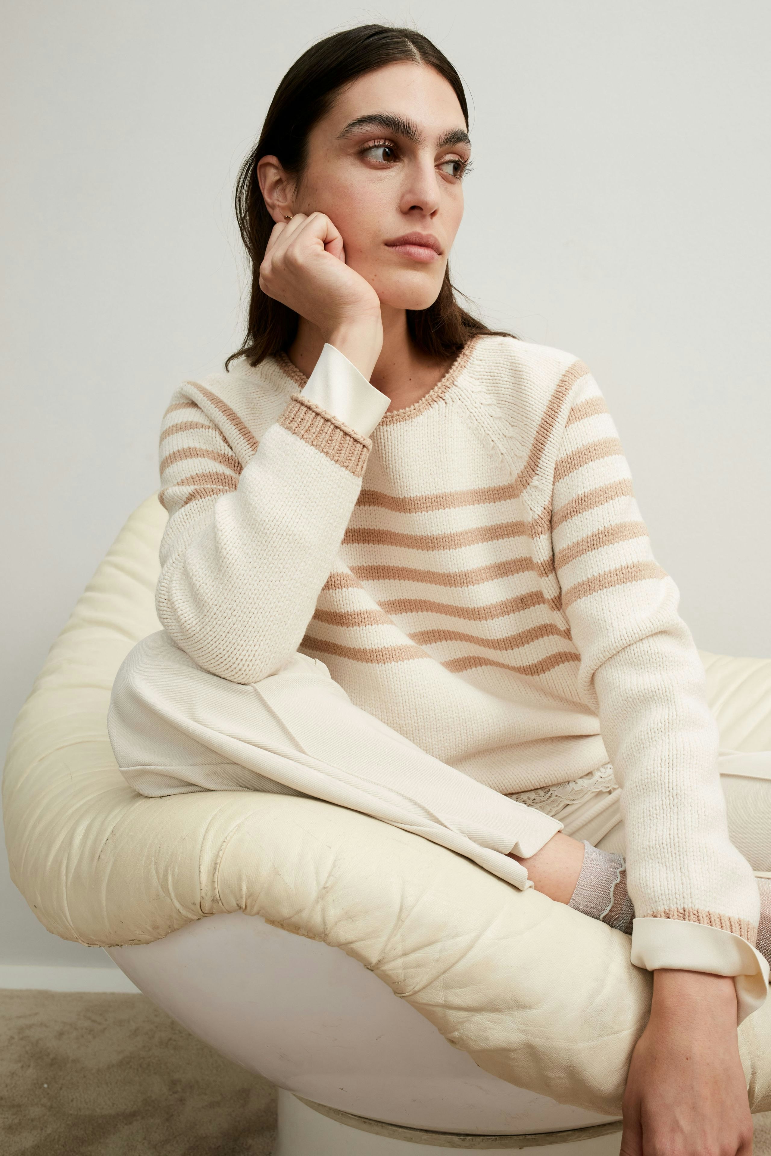 Damen-Pullover: Frau in gestreiftem Pullover mit lässigem Schnitt sitzt entspannt auf einem Sessel.