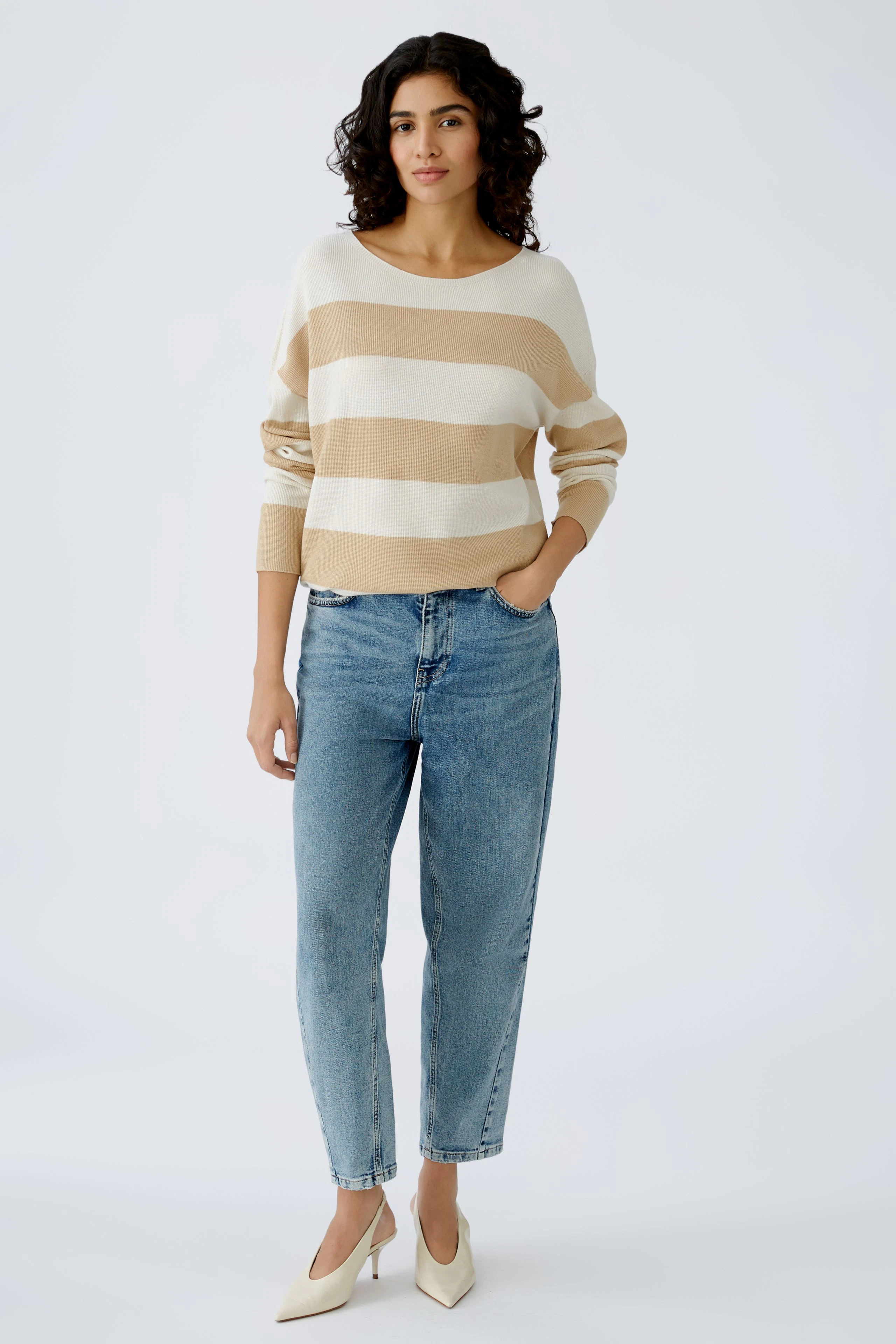Stylish women's pullover: A woman in a striped beige and white pullover paired with jeans.