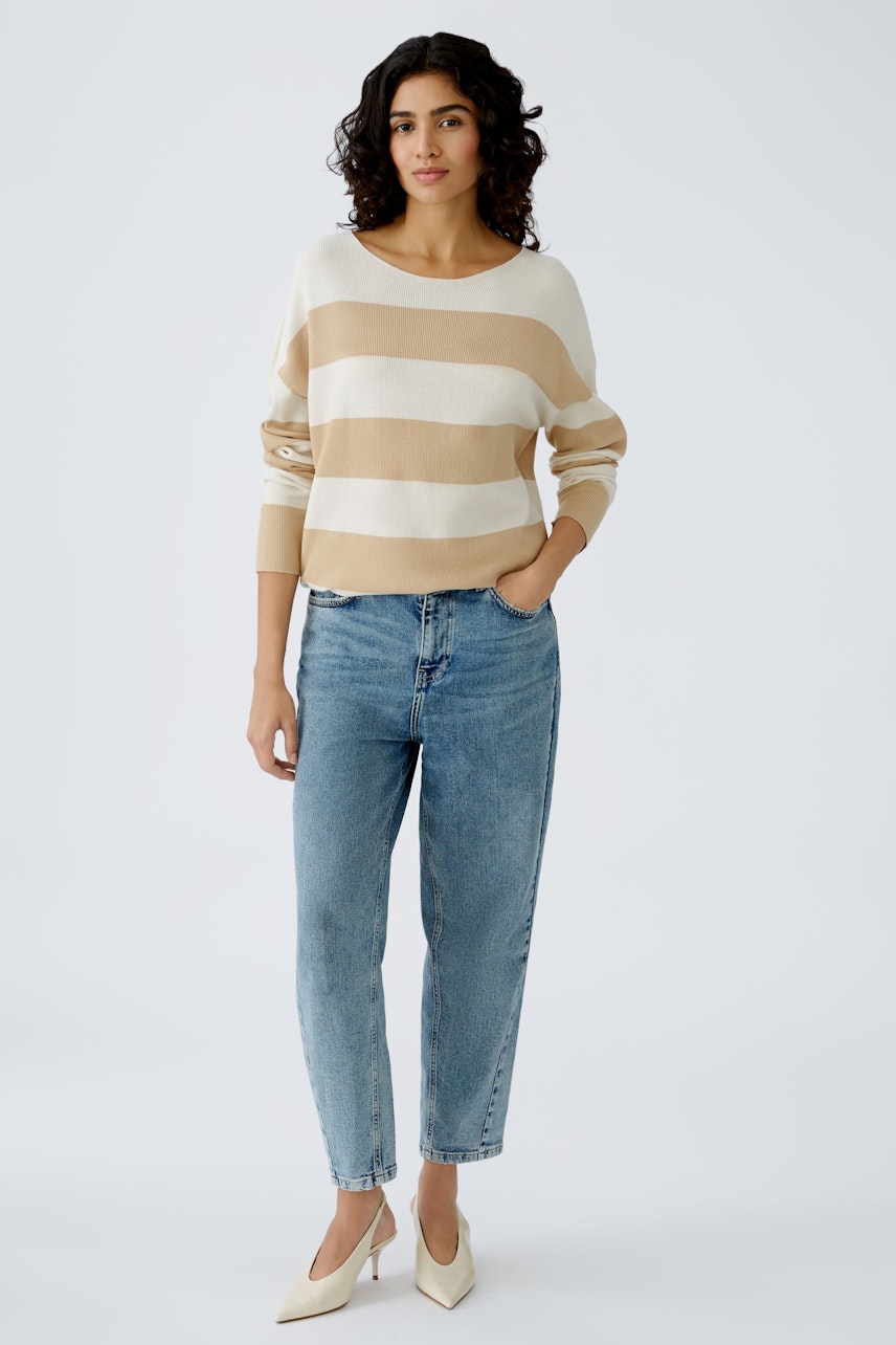 Stylish women's pullover: A woman in a striped beige and white pullover paired with jeans.