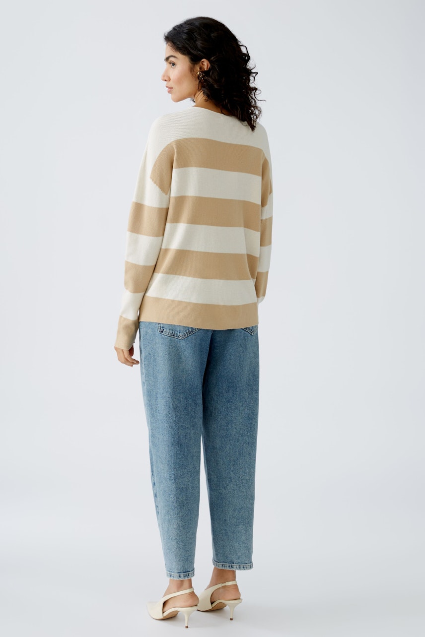 Stylish women's pullover: A woman in a striped pullover with beige and white tones, paired with relaxed jeans.