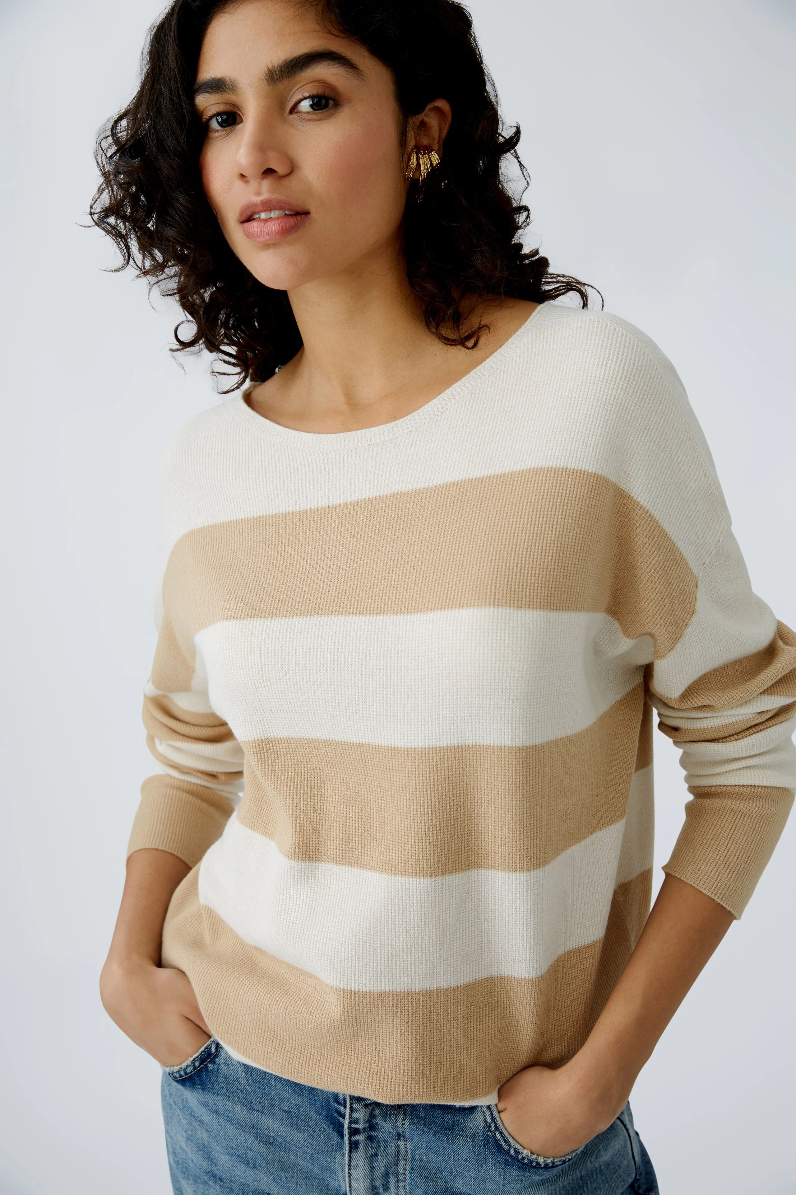 Modern women's pullover: A woman in a striped pullover with beige and white tones, looking confidently.