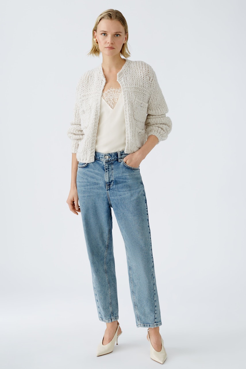 Stylish women's cardigan: A woman in a cozy cream cardigan over a light top and jeans, exuding effortless elegance.