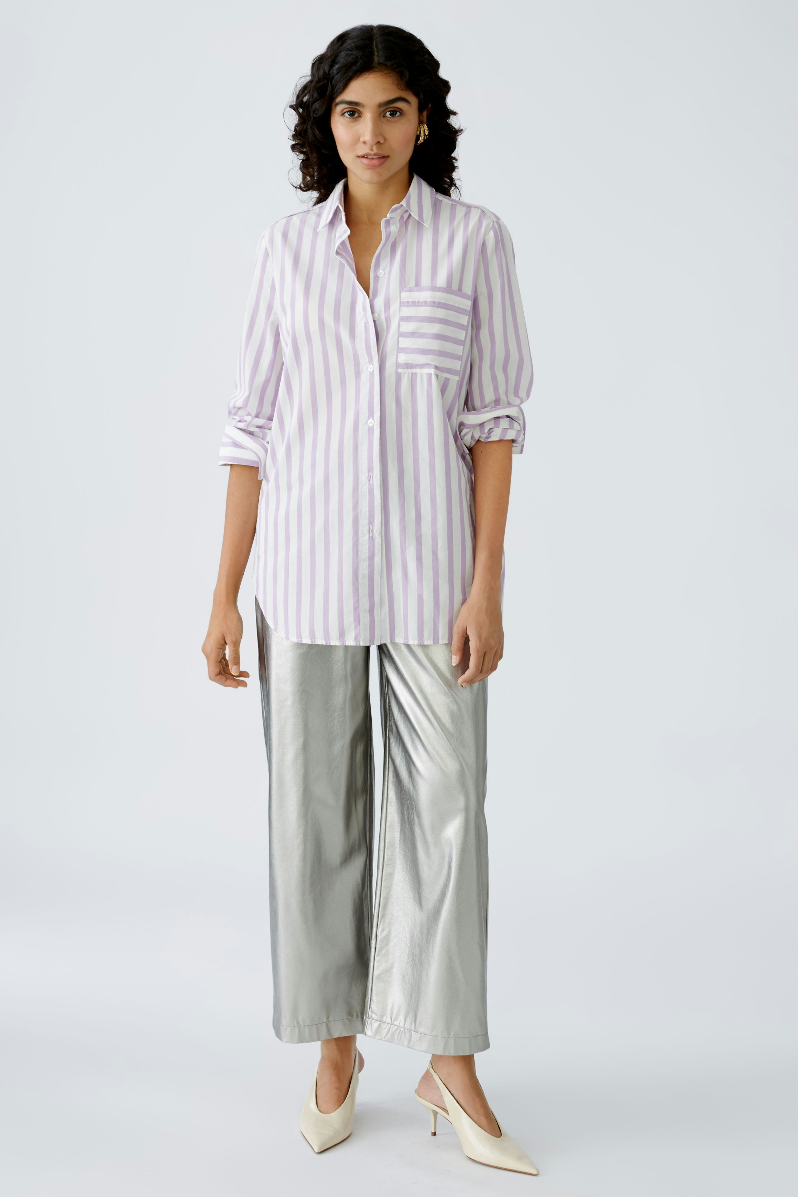Stylish women's blouse: A woman in a striped shirt with a pocket, paired with shiny silver pants.