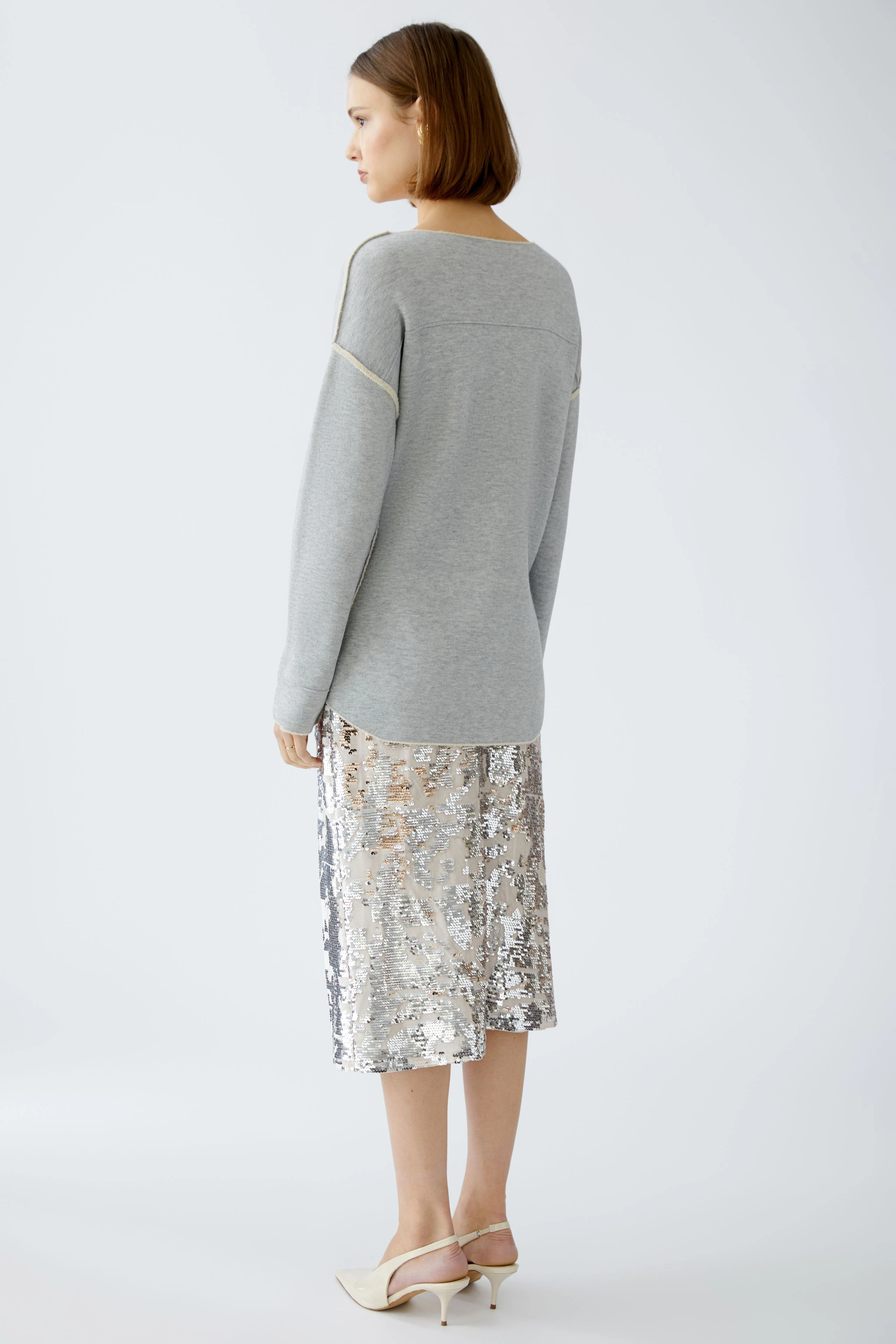 Damen-Pullover: Frau in grauem Pullover mit eleganter, glitzernder Rockkombination von hinten.