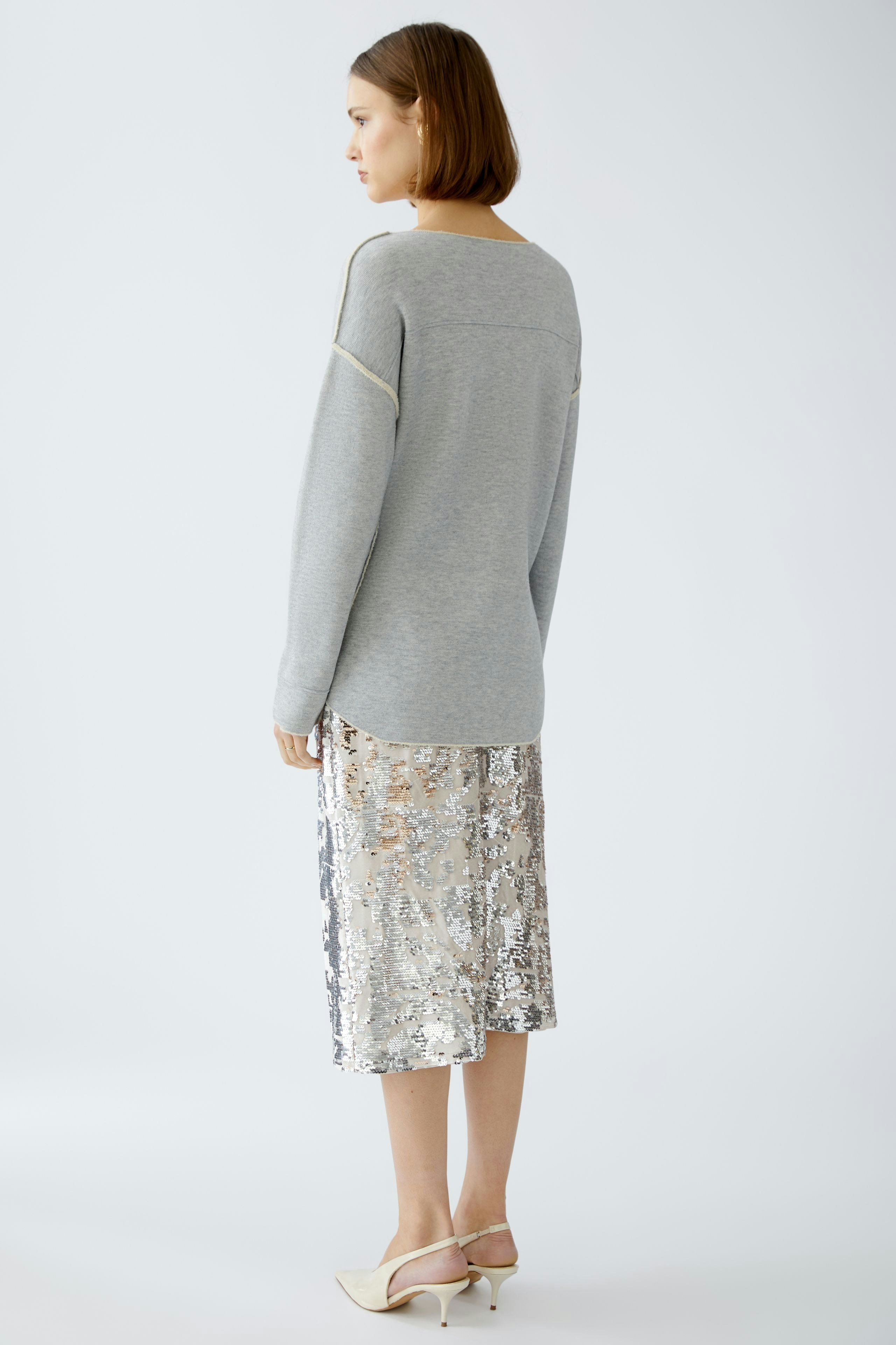 Stylish women's pullover: A woman in a light gray pullover paired with a shimmering silver skirt.