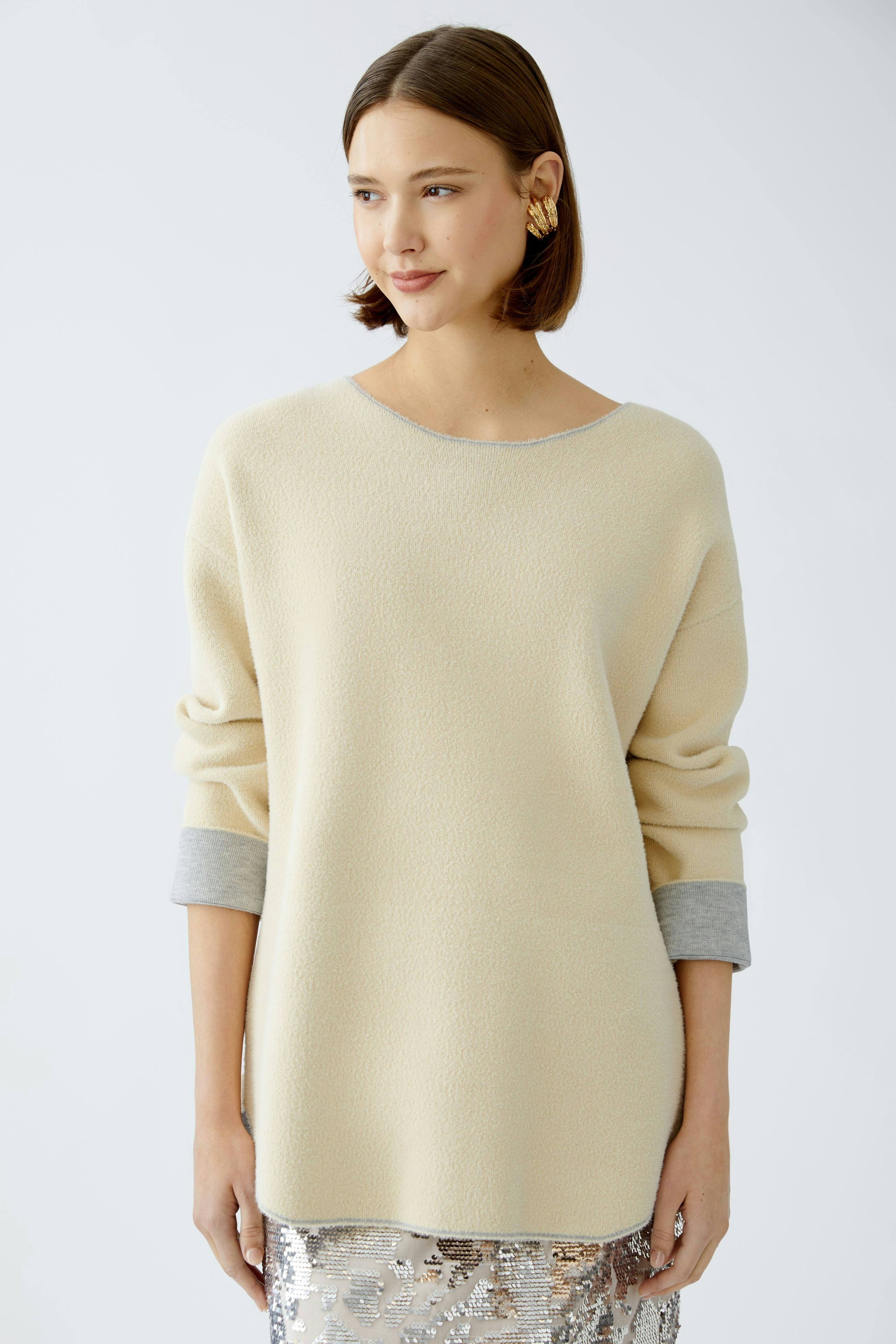 Modern women's pullover: A woman in a cream pullover with gray cuffs, exuding effortless style.