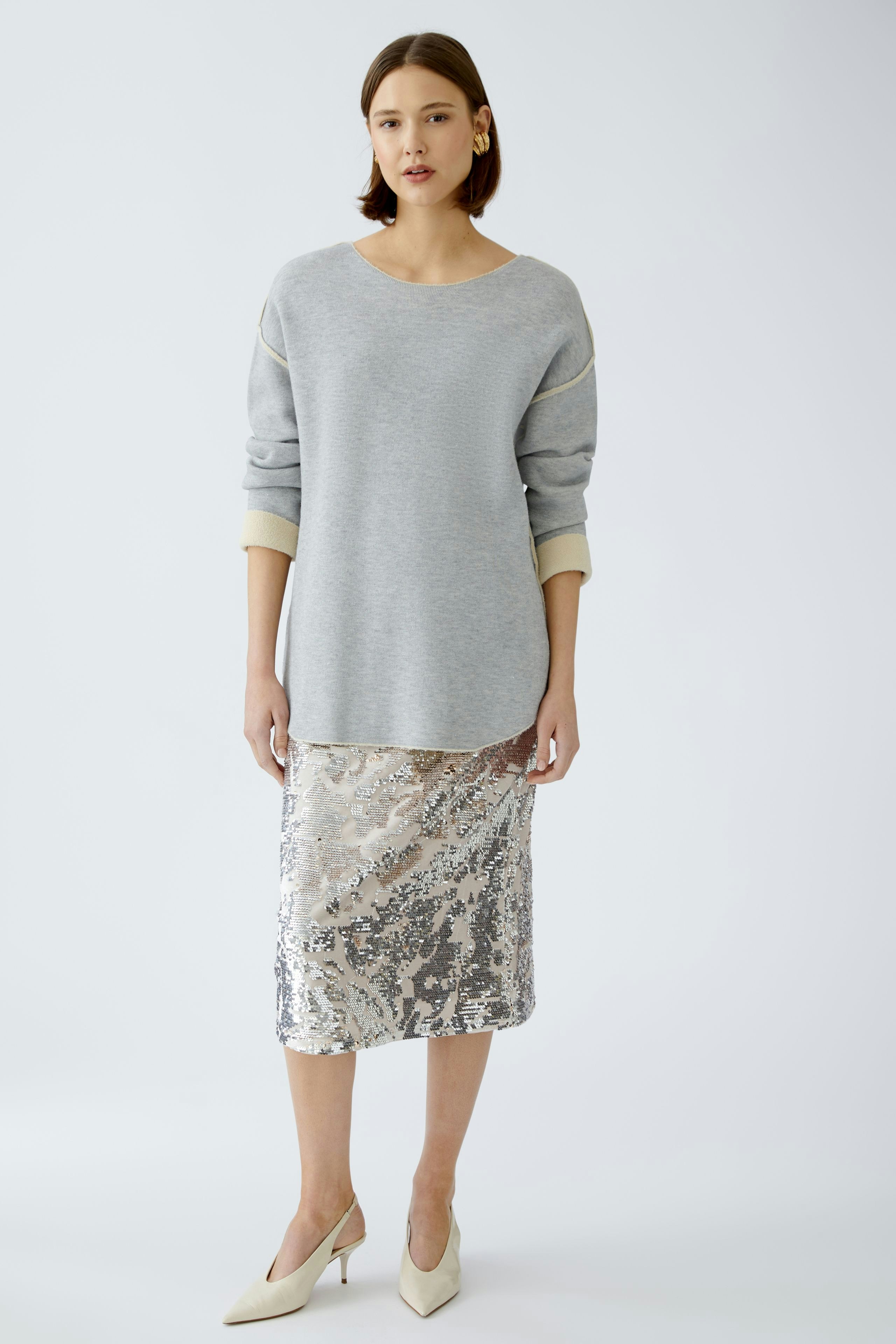 Stylish women's pullover: A woman in a light gray pullover with a relaxed fit, paired with a sequined skirt.