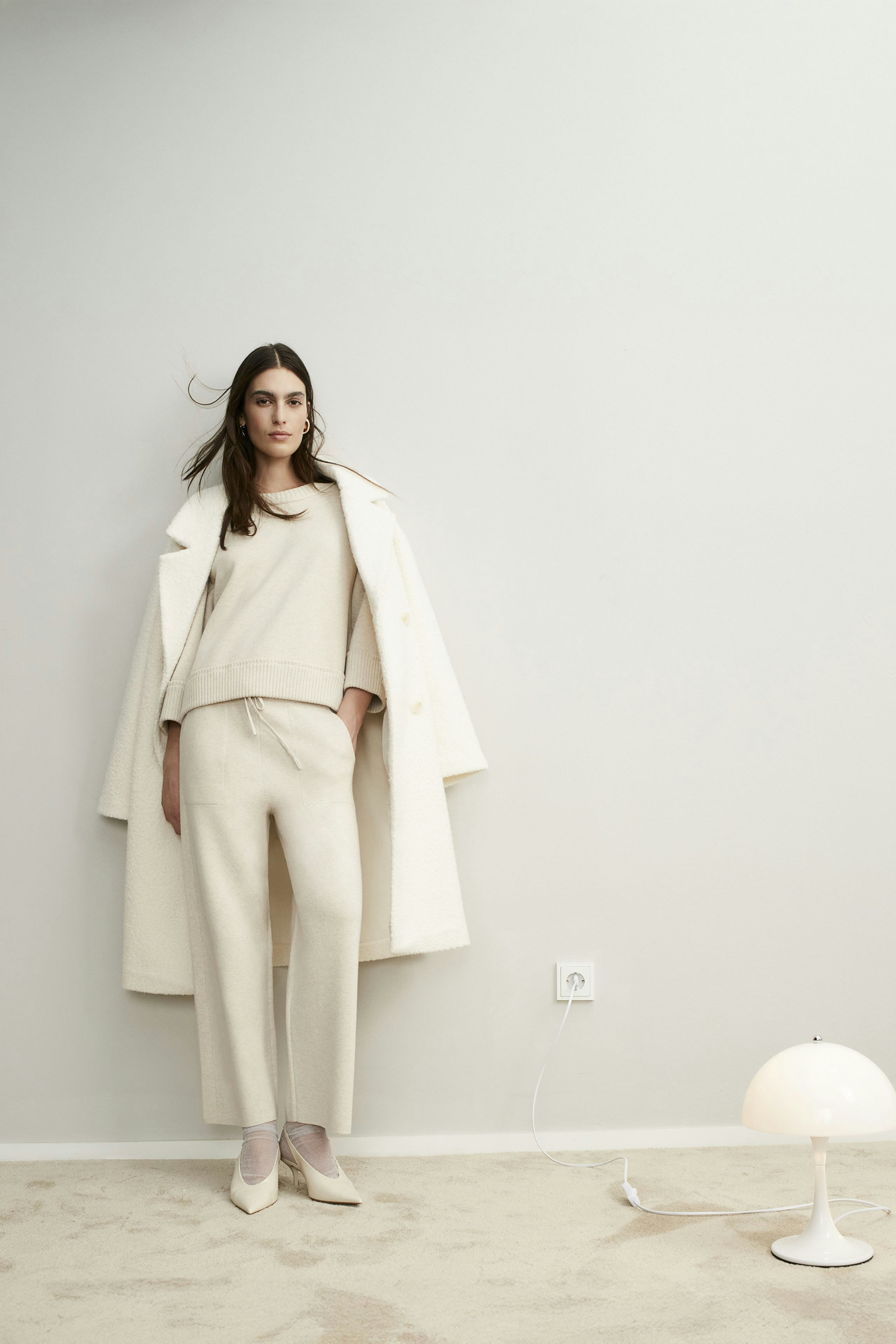 Eleganter Damen-Pullover: Frau in hellem Pullover und schimmerndem Rock steht stilvoll vor neutralem Hintergrund.