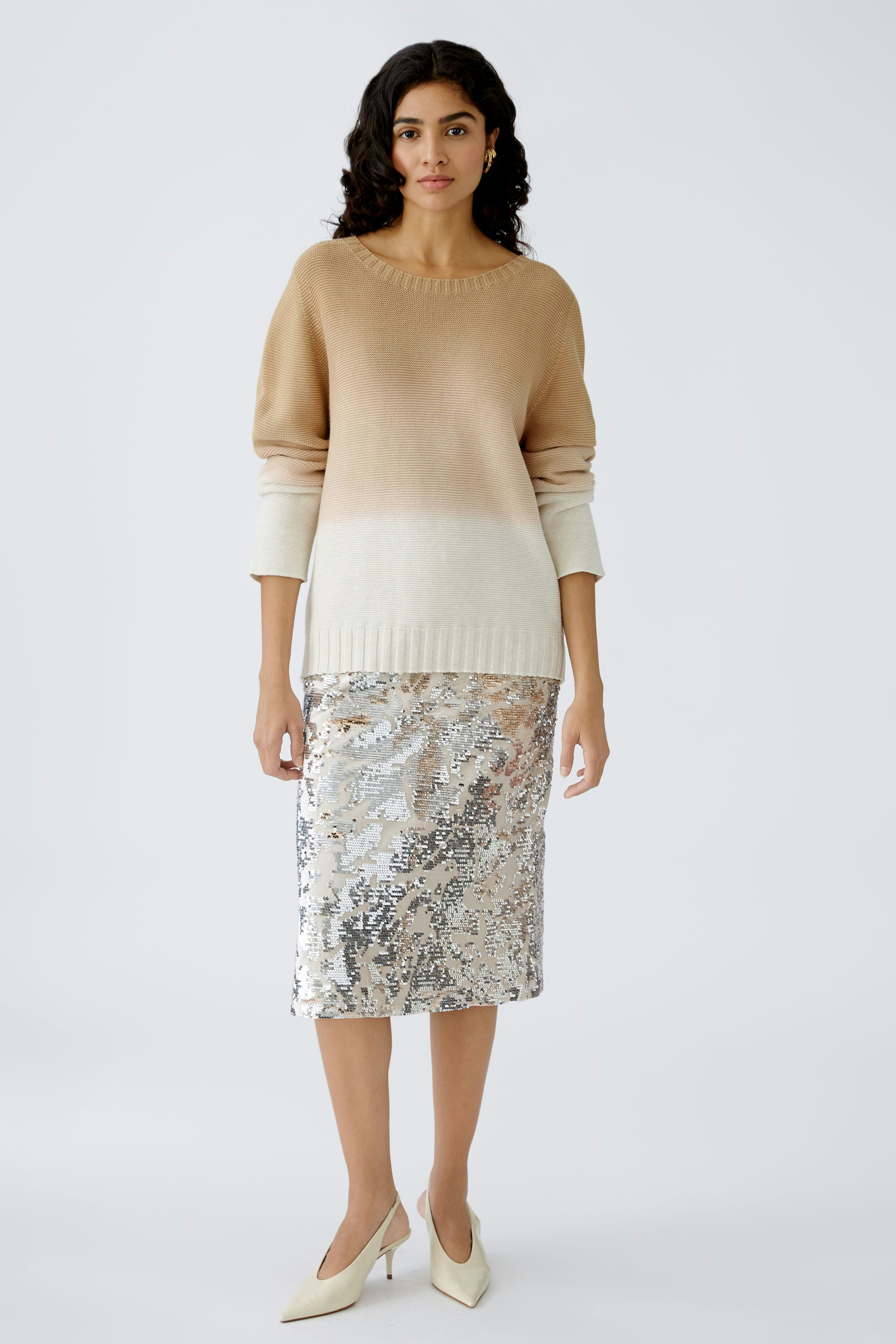 Stylish women's pullover: A woman in a beige ombre pullover paired with a shimmering silver skirt.