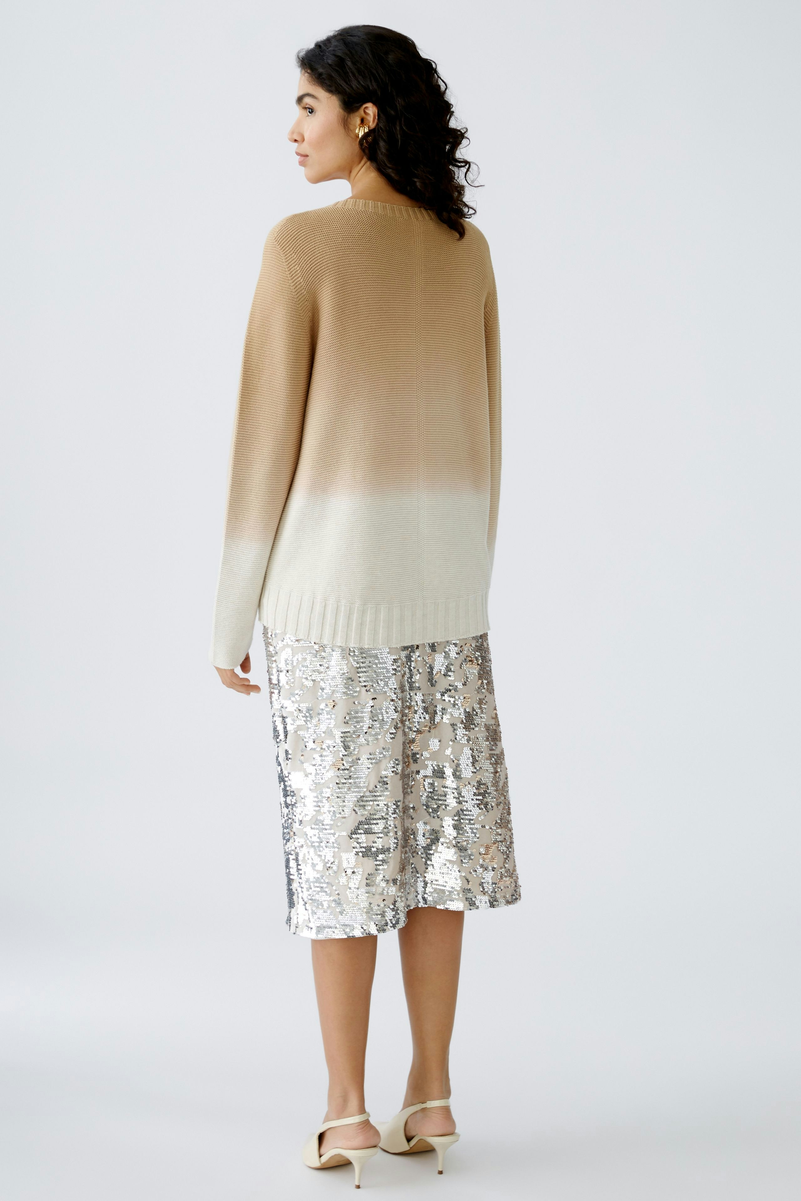 Elegant women's pullover: A woman in a gradient beige pullover paired with a shimmering silver skirt.