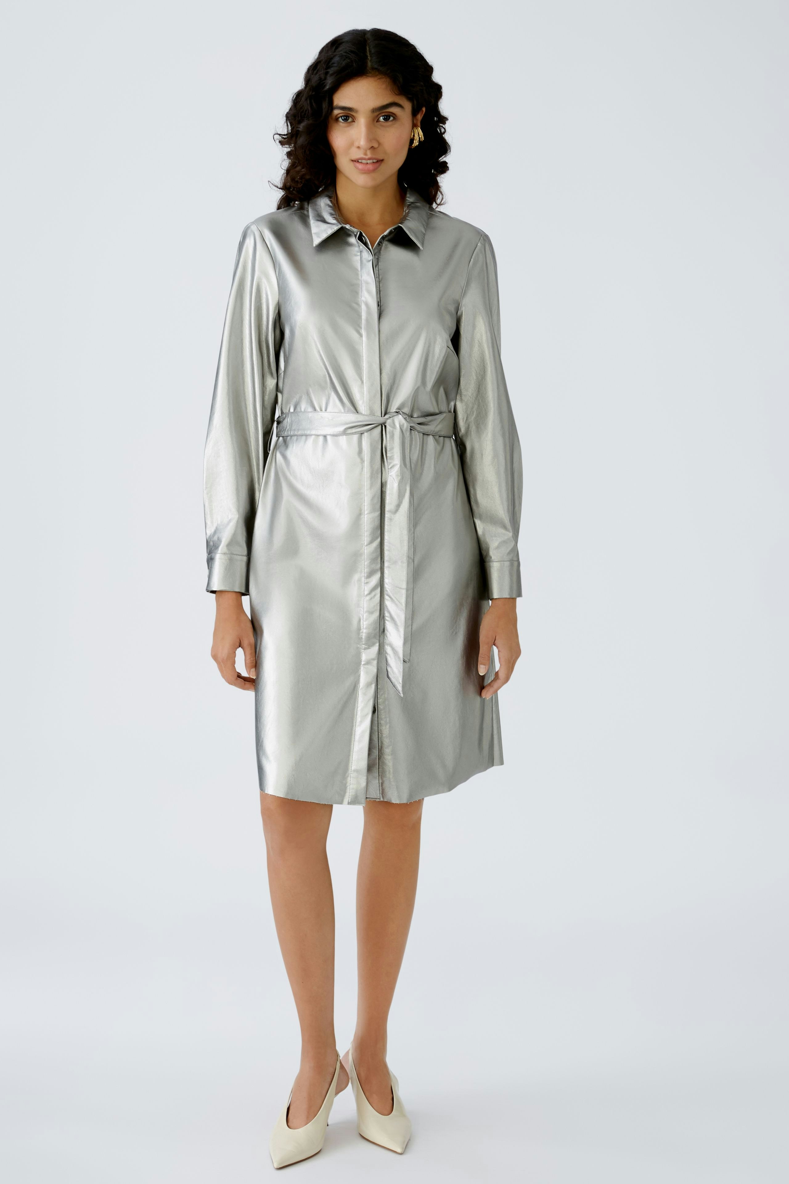 Shiny silver shirt dress: A woman in a sleek, metallic dress with a belted waist and elegant collar.
