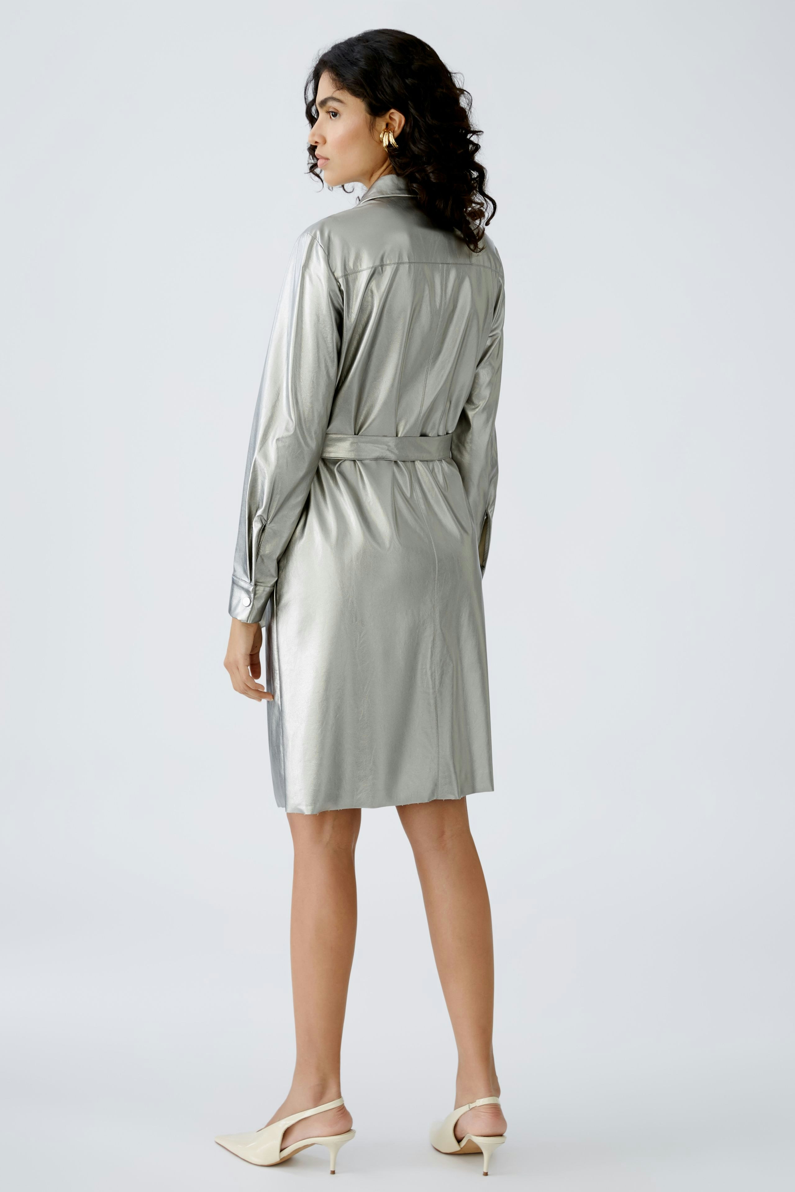 Stylish shirt dress: A woman in a shiny silver shirt dress with a belted waist, showcasing modern elegance.