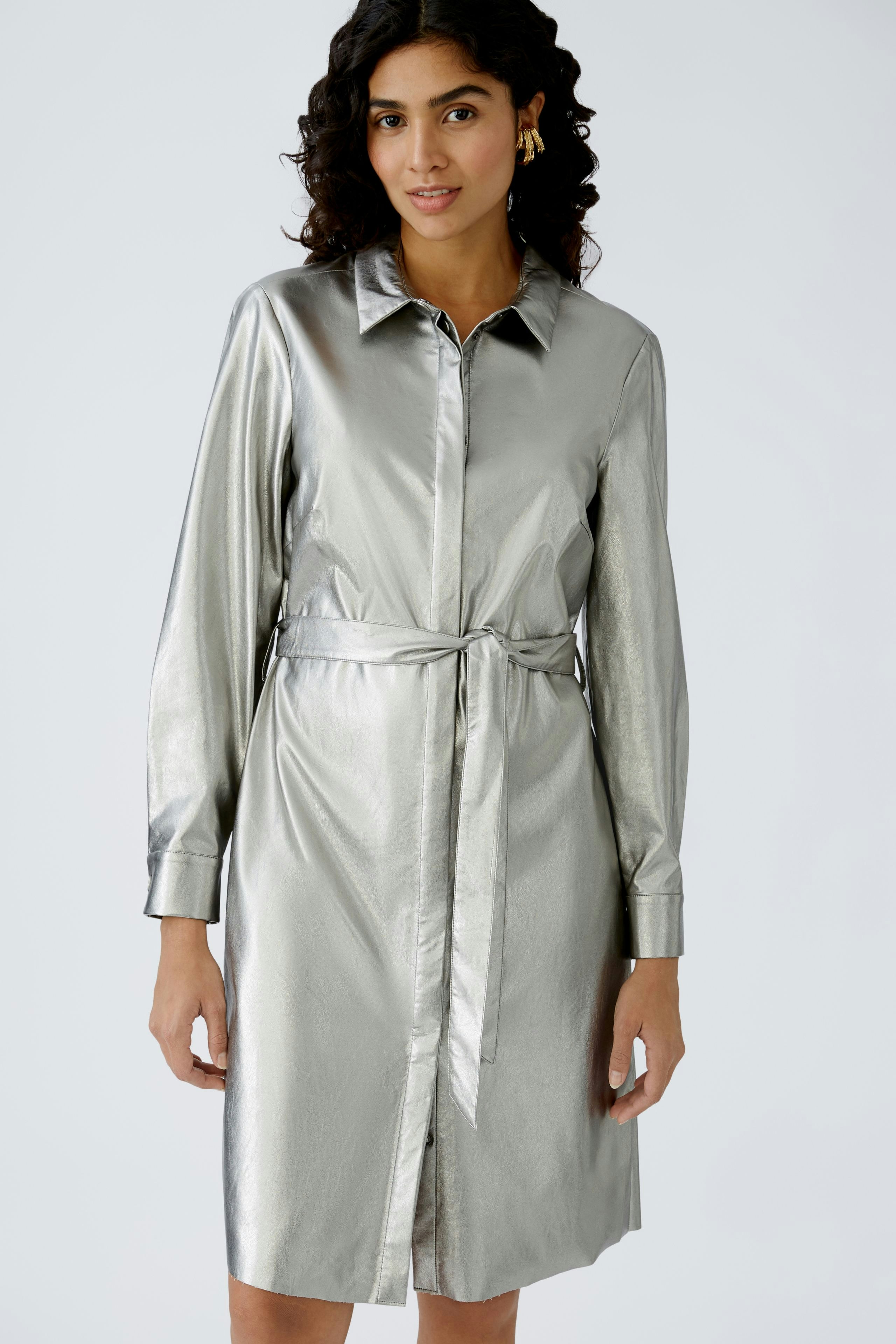 Shiny shirt dress: A woman in a silver shirt dress with a tie waist, exuding elegance and style.