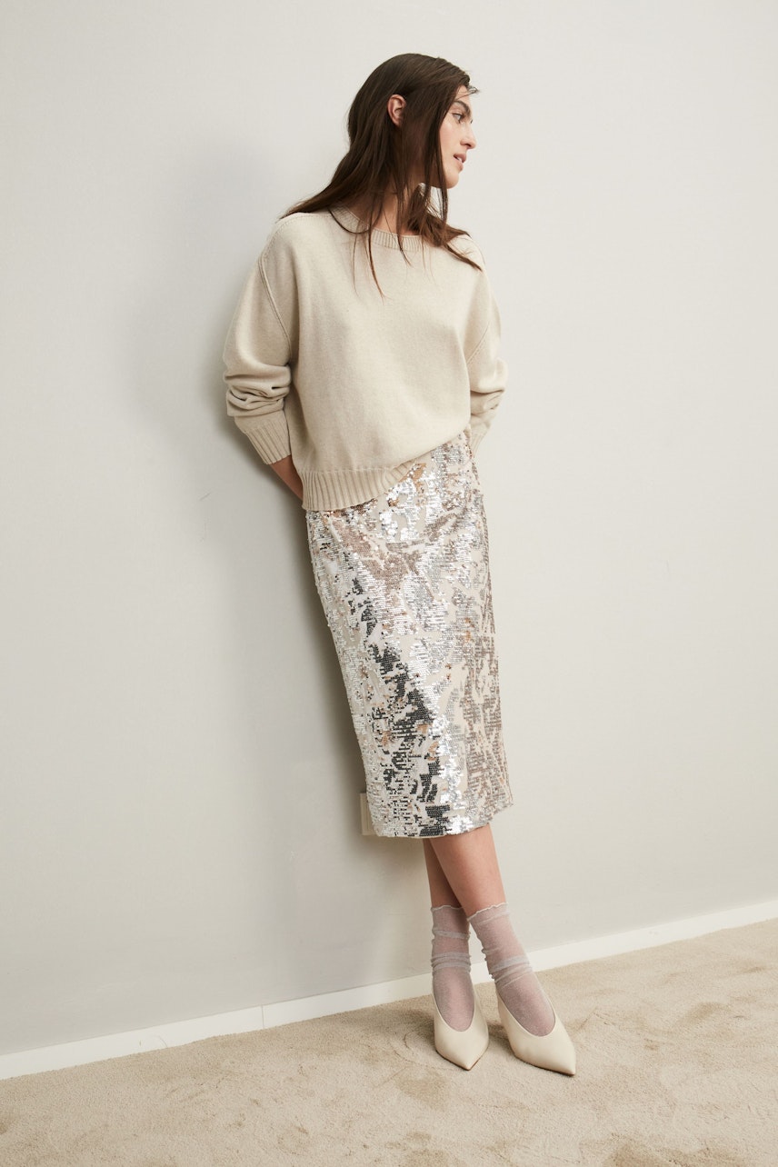 Elegant pencil skirt: A woman in a shimmering silver pencil skirt paired with a cozy beige pullover.