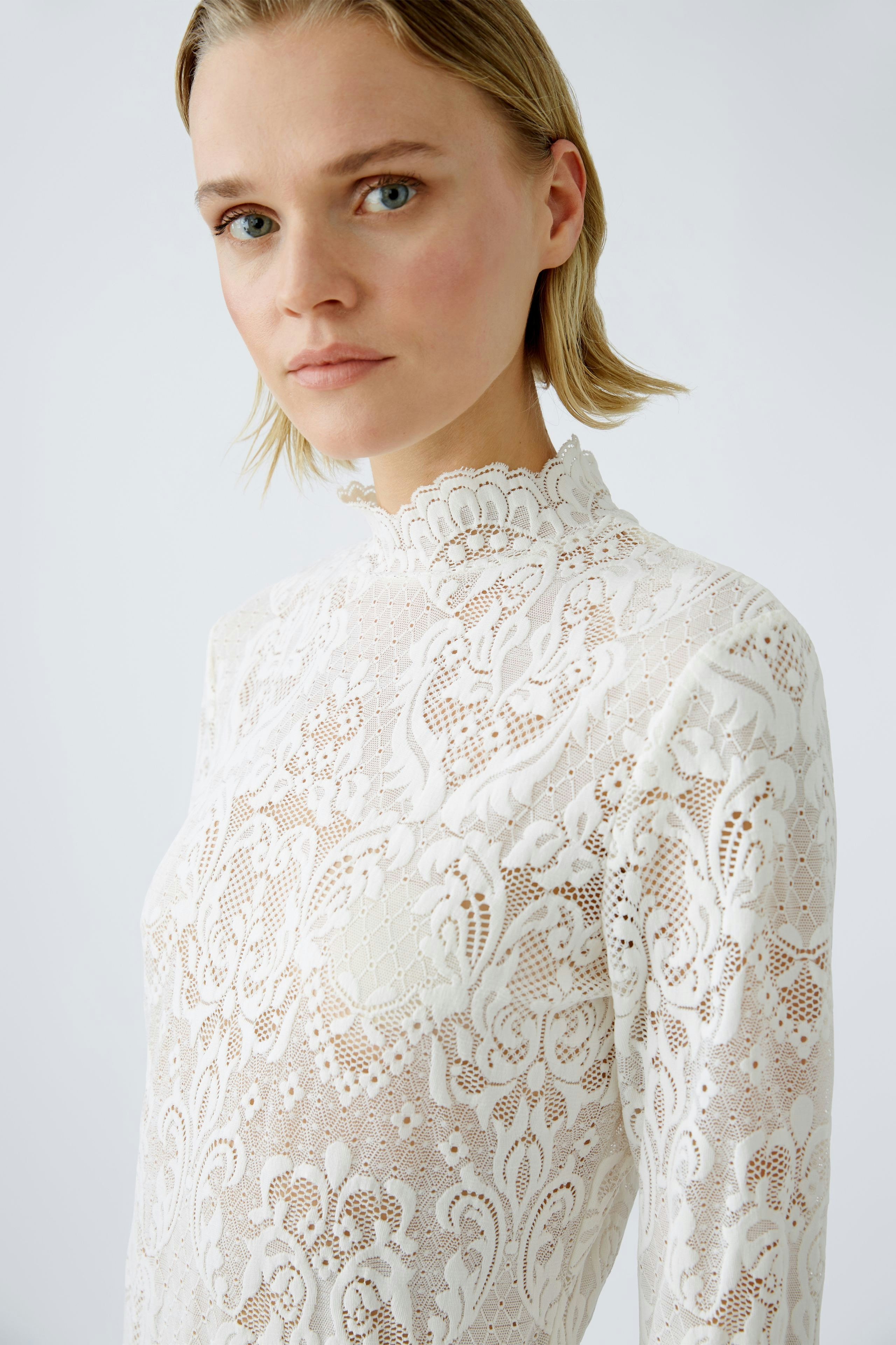Elegant long-sleeve shirt: Woman in a white lace top with a high neckline, showcasing intricate details.
