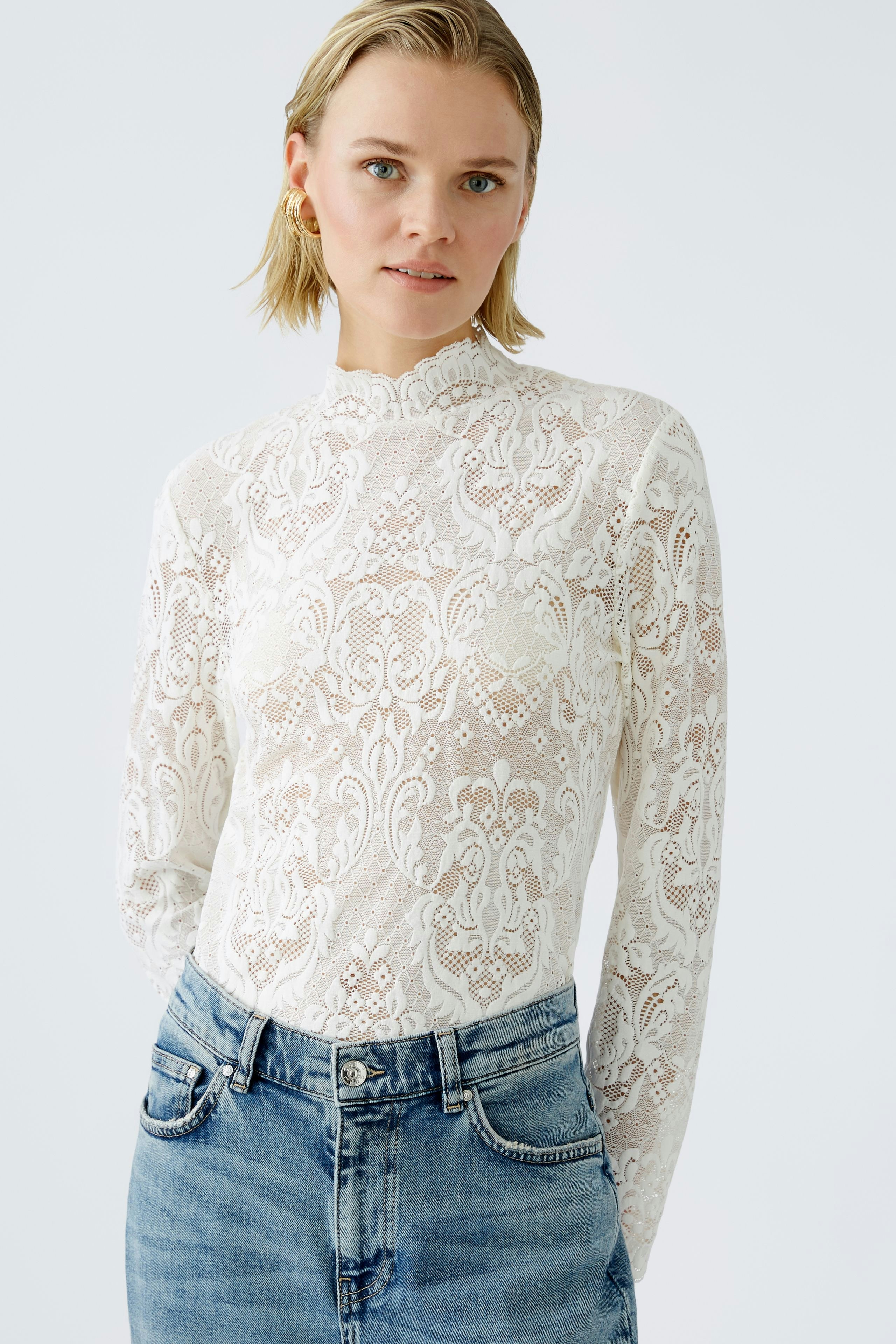 Elegant long-sleeve shirt: Woman in a white lace top paired with denim, exuding a chic style.