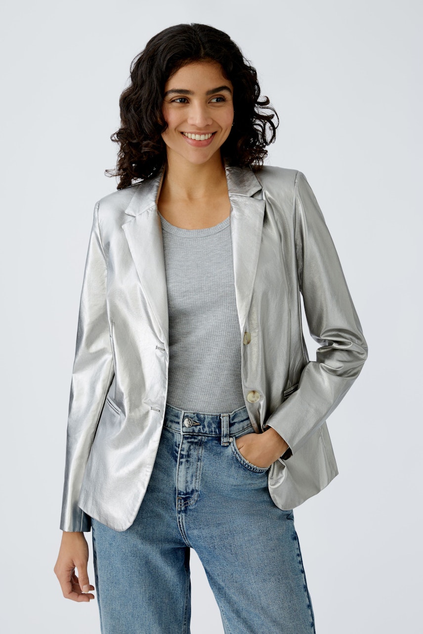 Stylish women's blazer: A woman in a shiny silver blazer paired with casual jeans, smiling confidently.