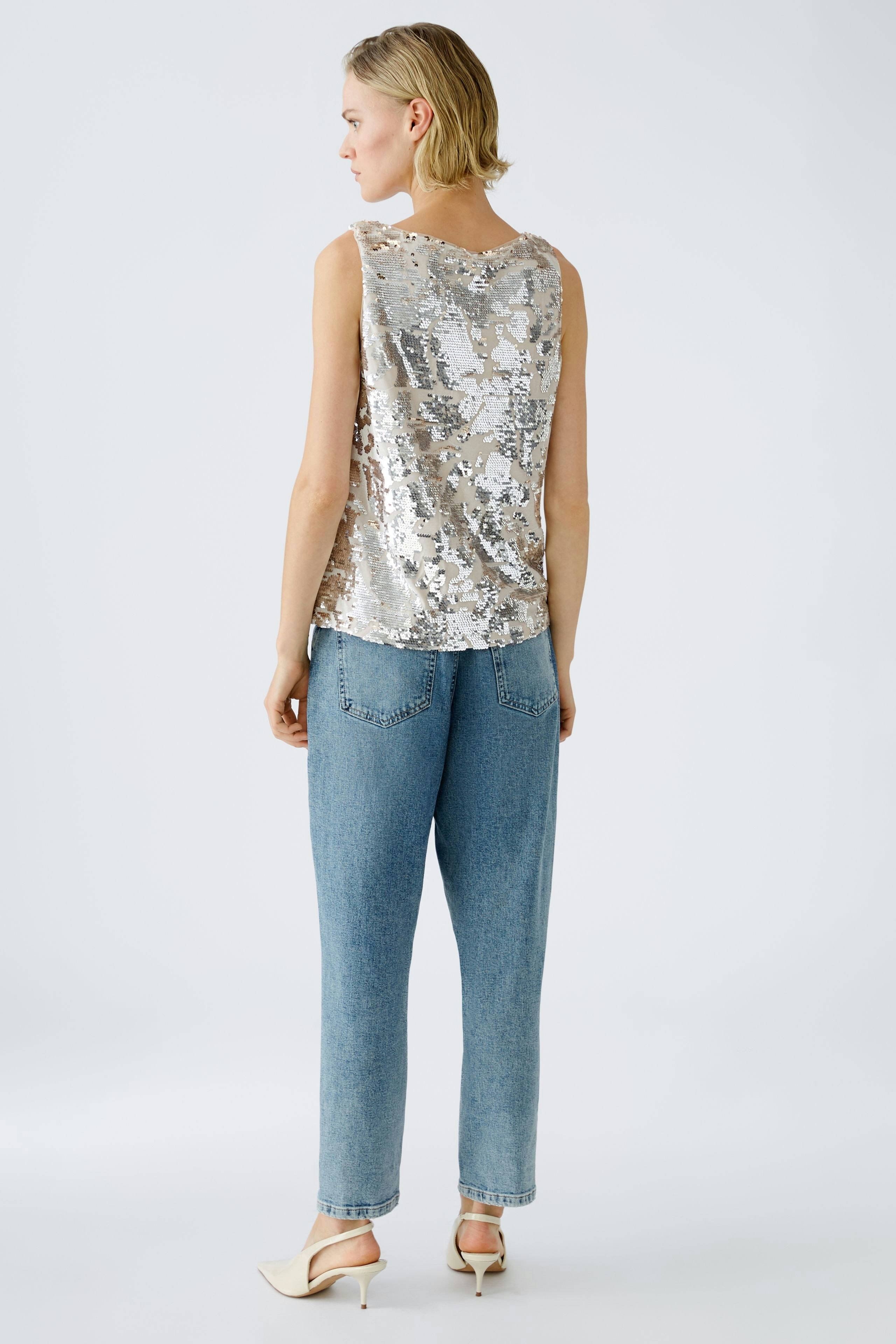 Stylish tank top: Woman in a shimmering silver sleeveless top paired with relaxed denim jeans.