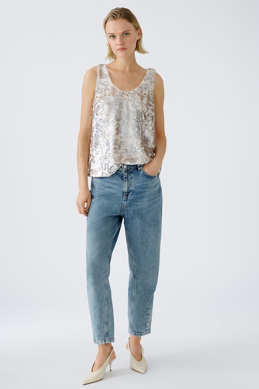 Stylish women's tank top: A woman in a shimmering silver tank top paired with blue jeans.