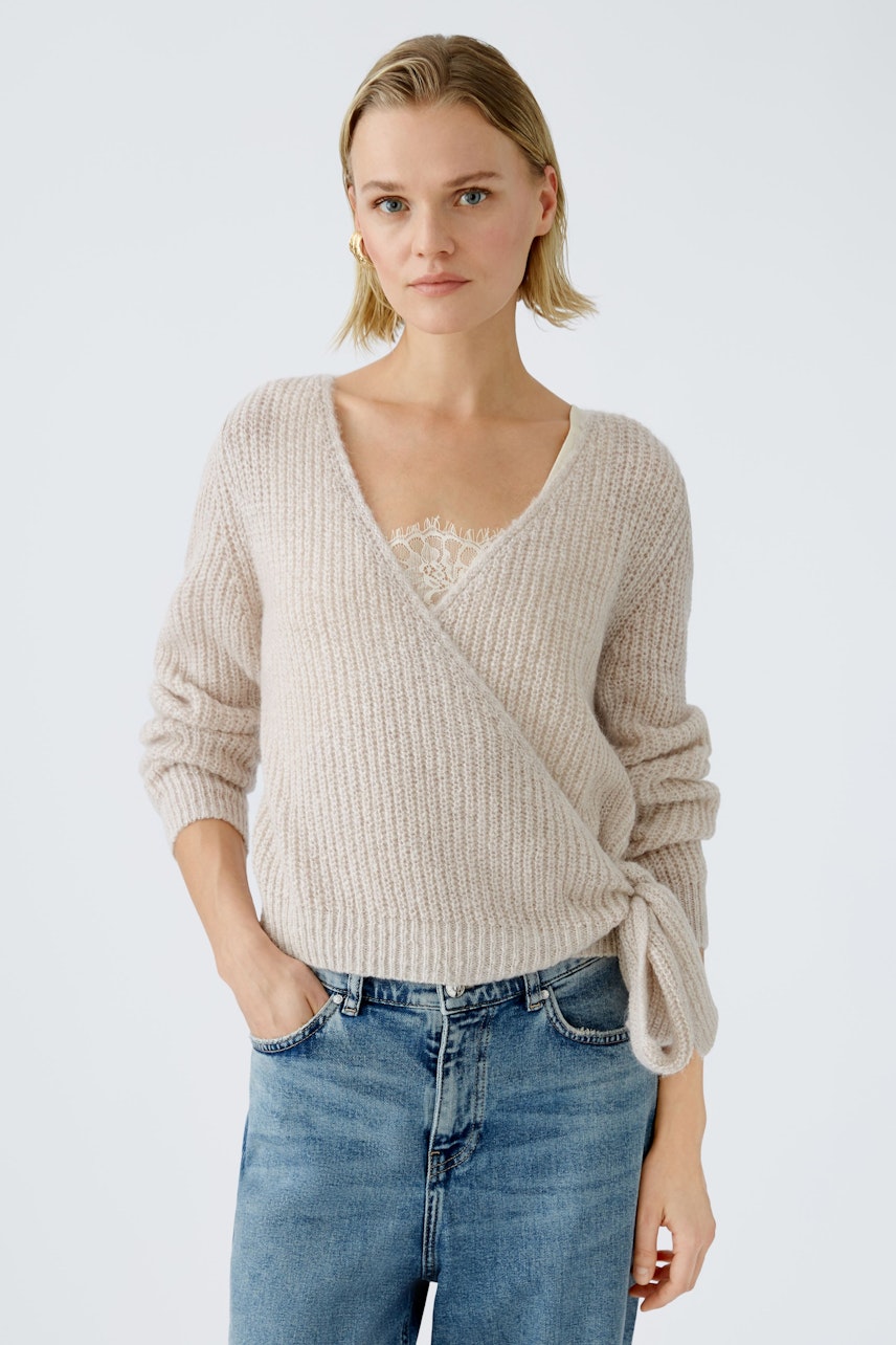 Stylish women's pullover: A woman in a soft beige wrap pullover paired with casual jeans.