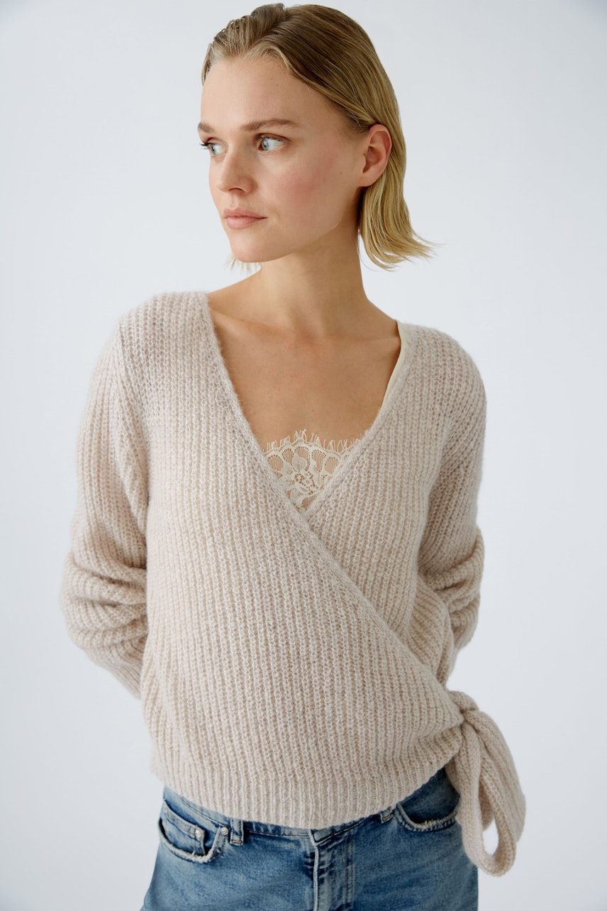 Stylish women's pullover: A woman in a soft beige wrap pullover with a delicate lace top underneath.