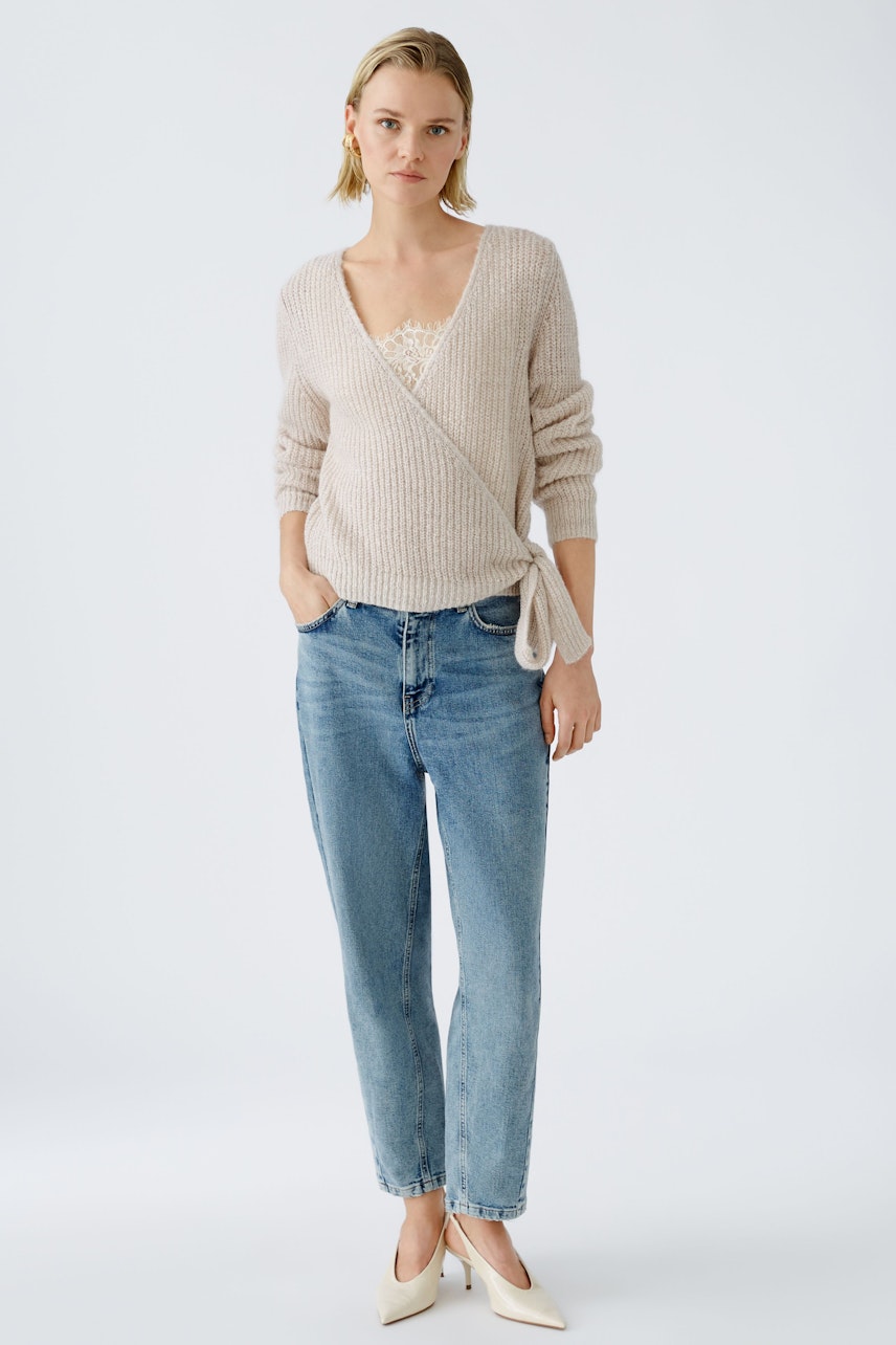 Stylish women's pullover: A woman in a soft beige wrap pullover paired with casual jeans.