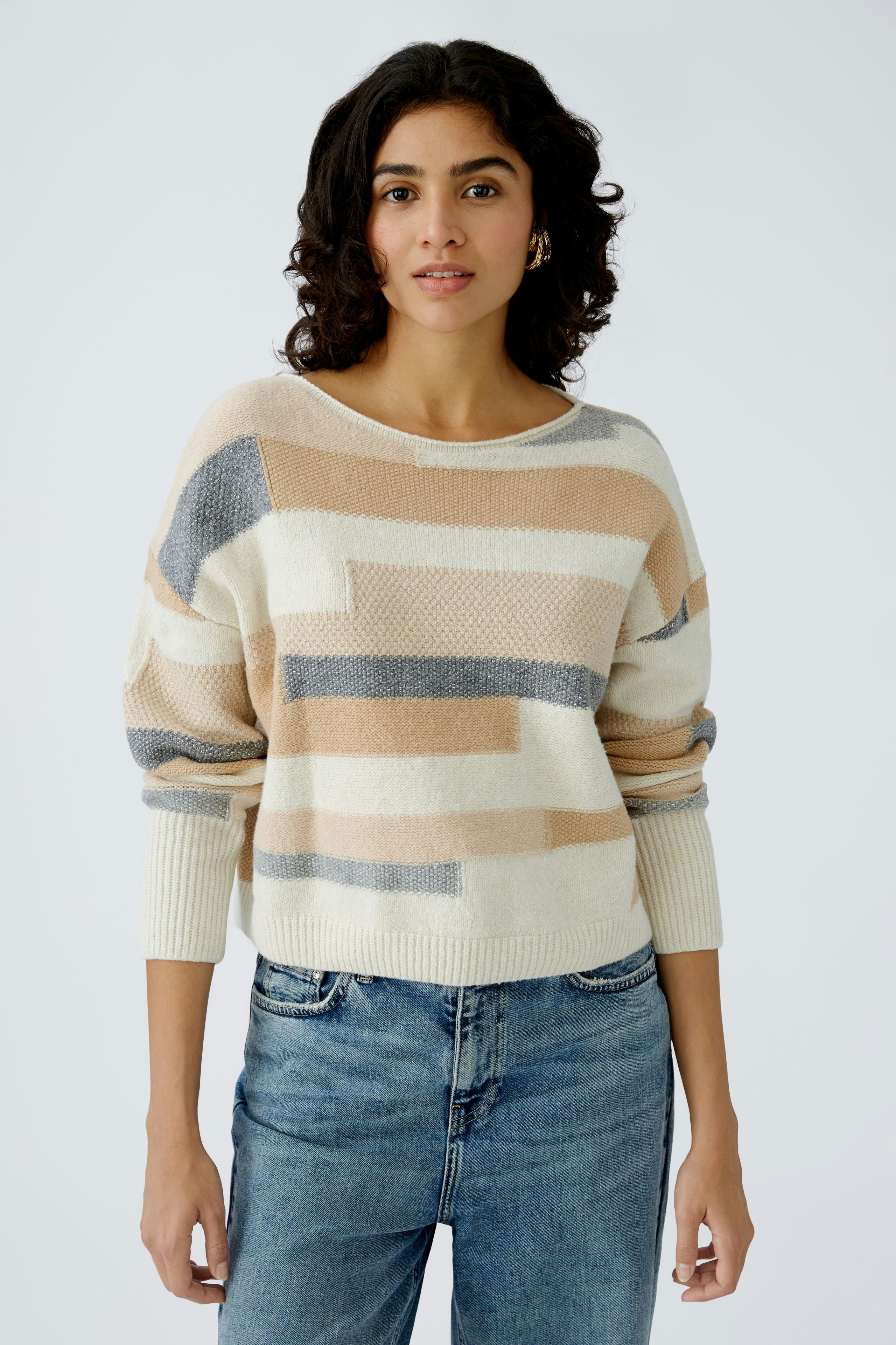 Stylish women's pullover: A woman in a cream pullover with geometric patterns and relaxed fit.