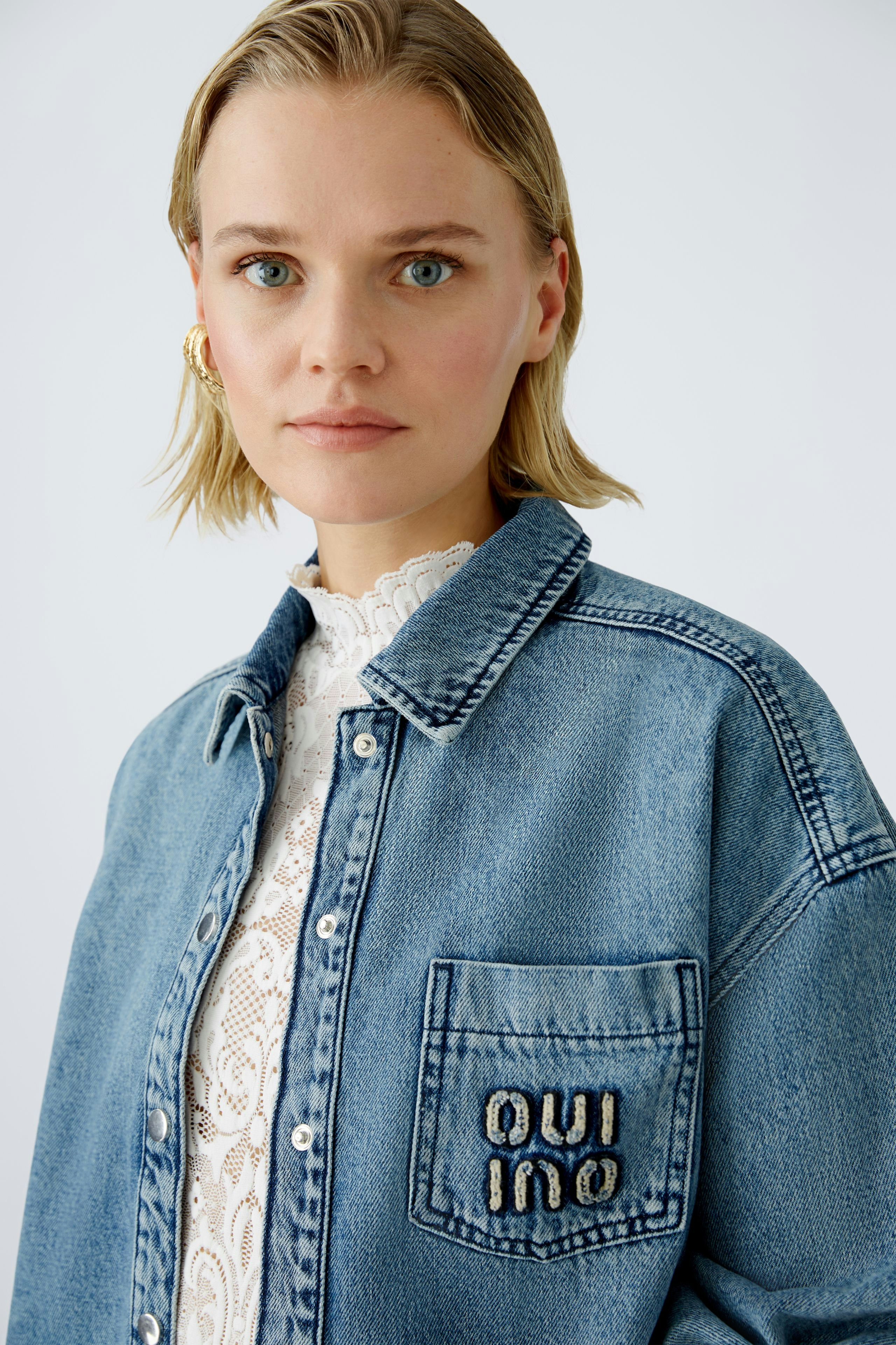 Stylish women's denim jacket: A woman in a blue jacket with embroidered logo, exuding casual elegance.
