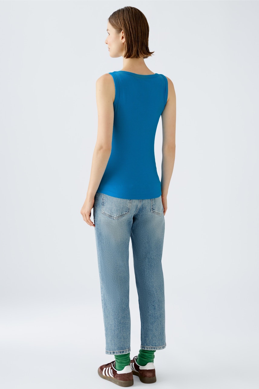 Elegantes Damen-Top: Frau in blauem ärmellosem Top und lässigen Jeans von hinten.