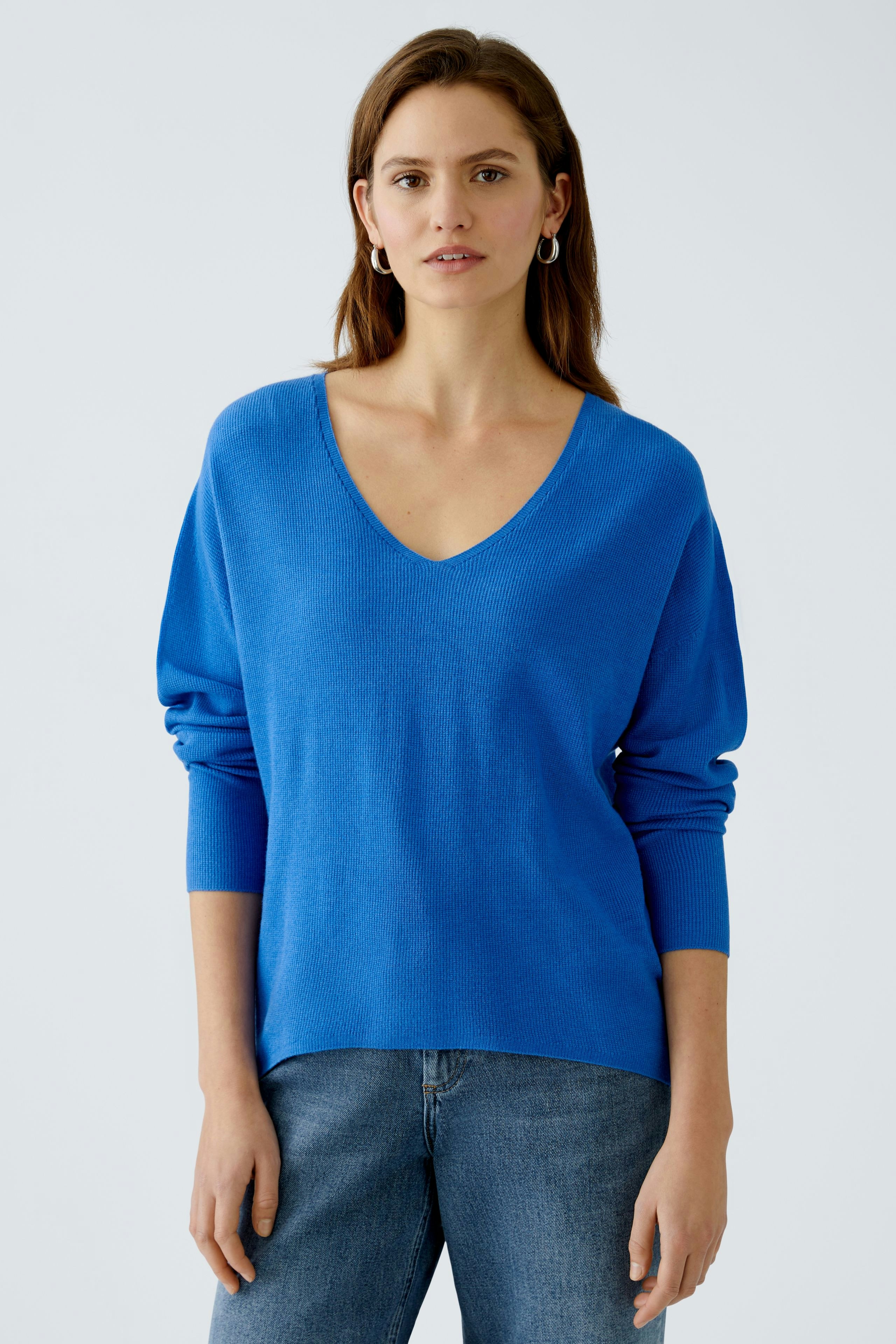 Stylish women's pullover: A woman in a vibrant blue V-neck pullover paired with casual jeans.