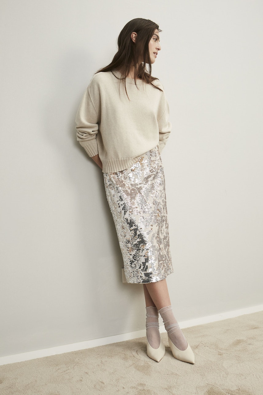 Stylish women's pullover: A woman in a cream pullover paired with a shimmering silver skirt.