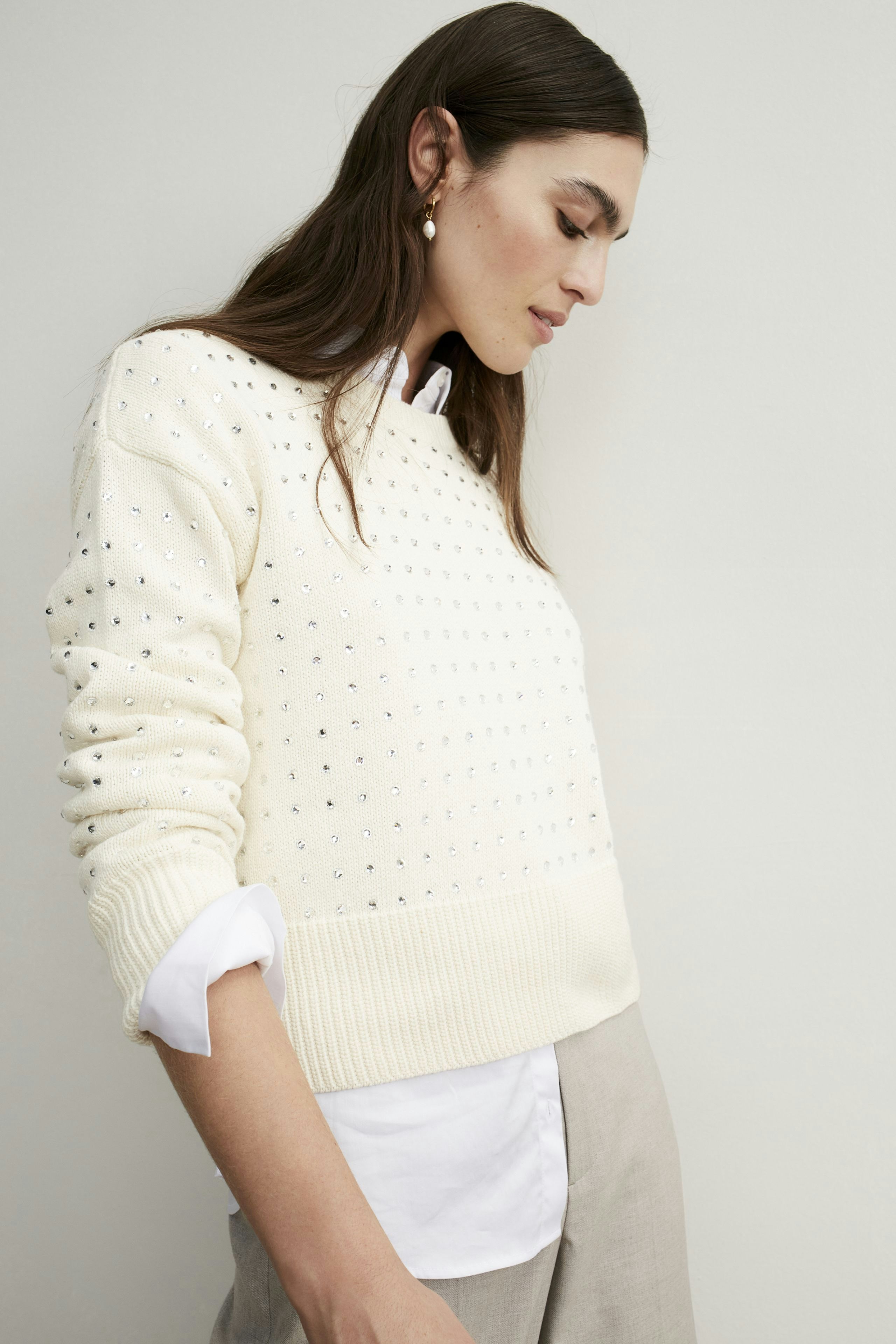 Stylish women's pullover: A woman in a cream pullover with subtle embellishments, paired with a white shirt.