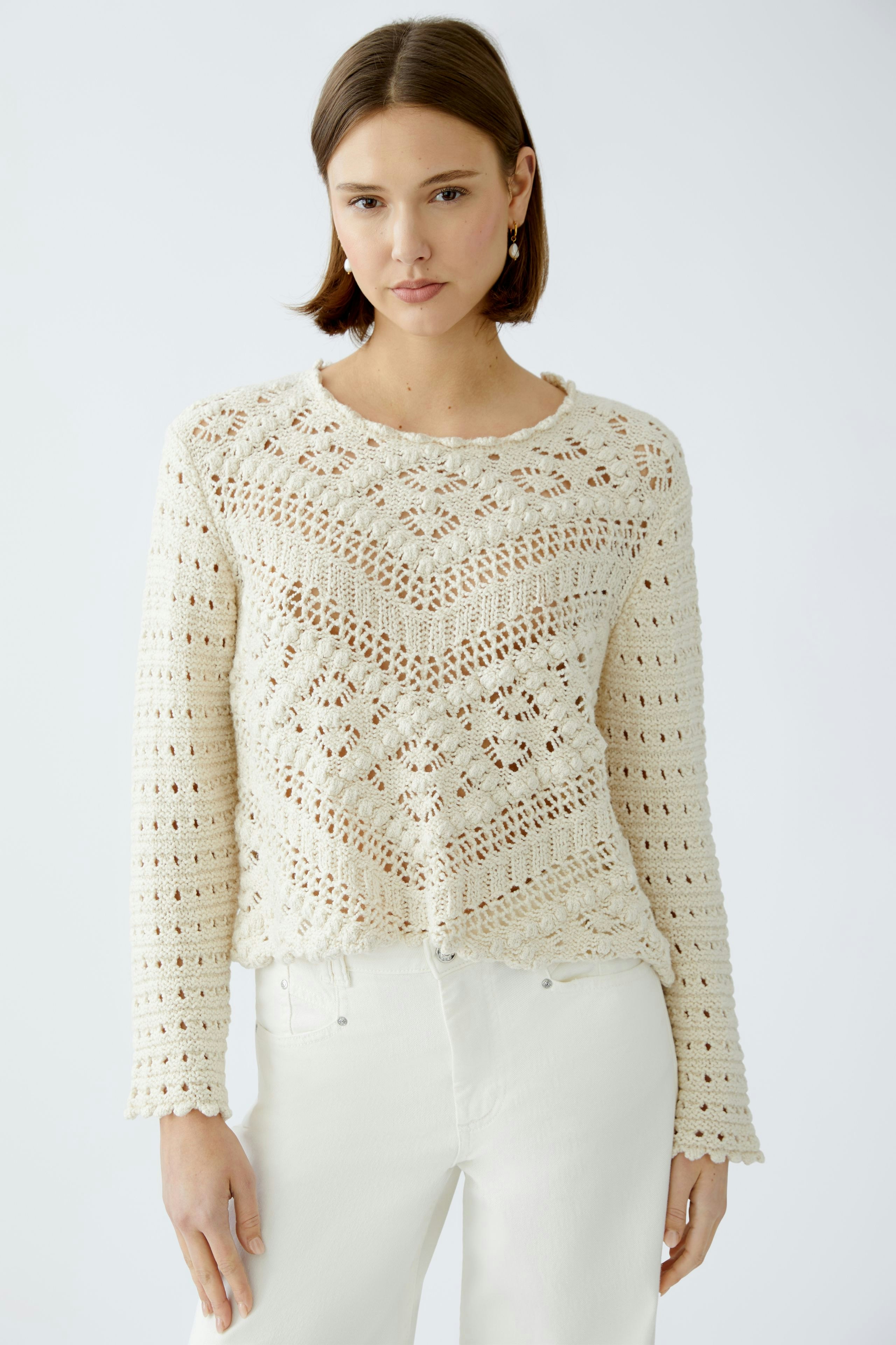 Stylish women's pullover: A woman in a cream crochet pullover paired with white jeans.