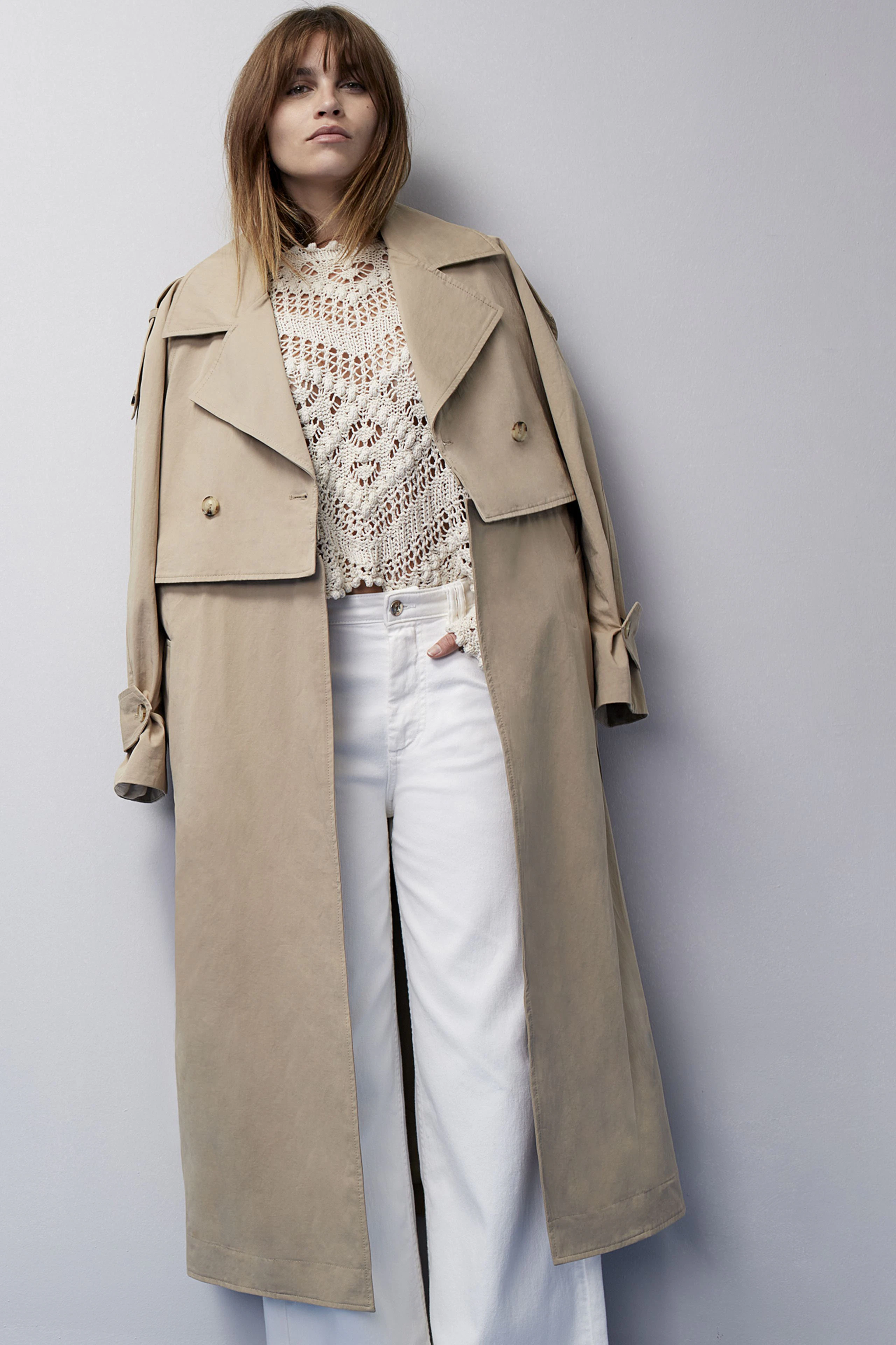Stylish women's pullover: A woman in a cream crochet pullover paired with a beige trench coat.