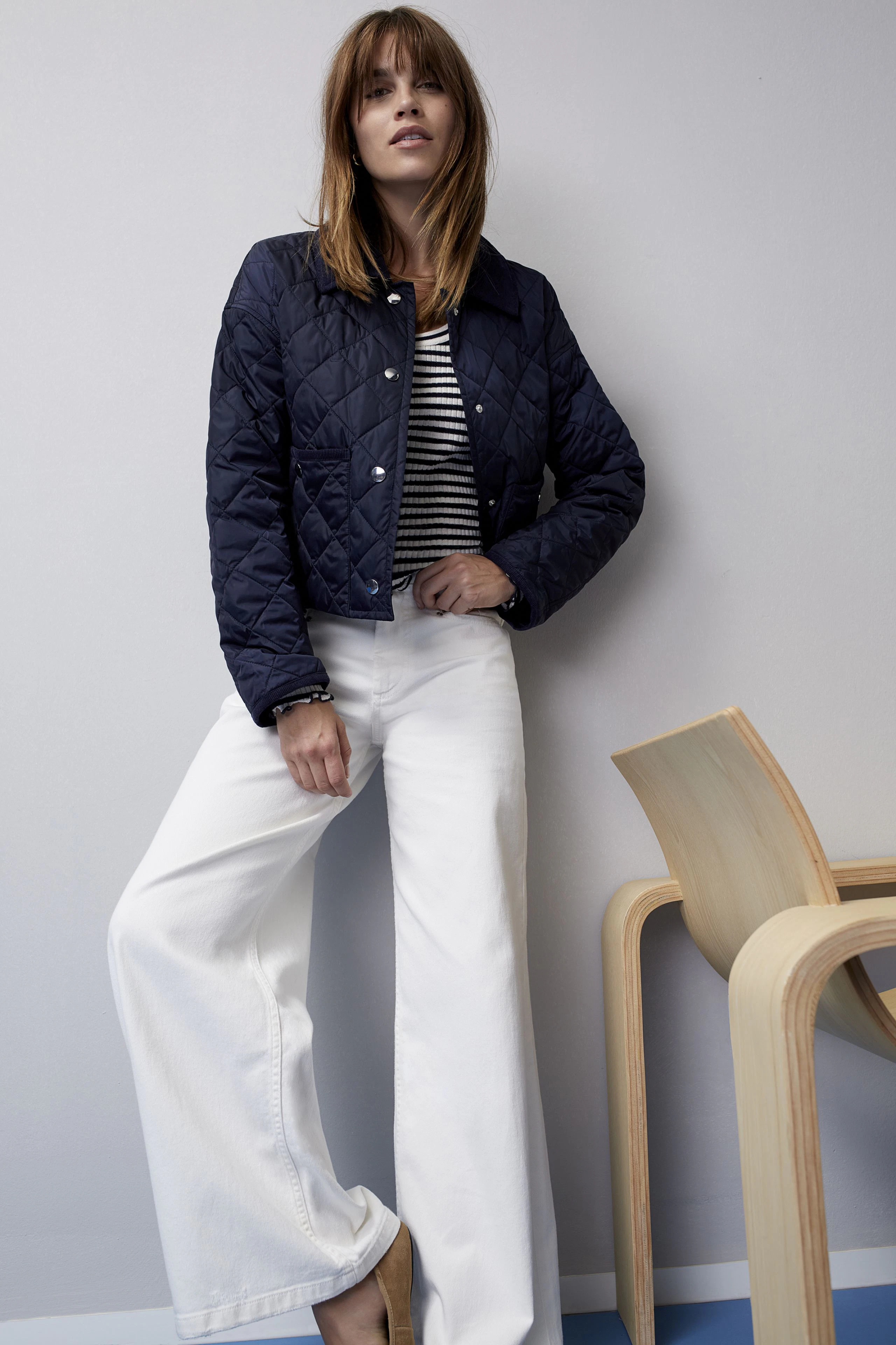 Stylish women's outdoor jacket: A woman in a navy quilted jacket over a striped top and white pants.